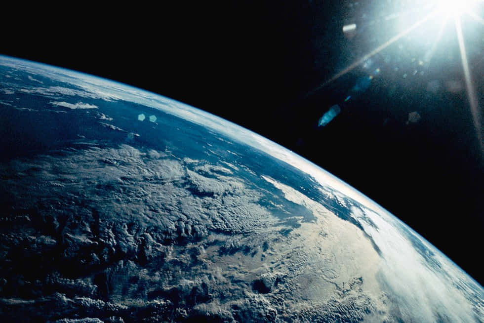 Outerspace 桌布 壁紙 — 地球在太空中雄偉地彎曲，太陽耀斑照亮了旋轉的雲層和海洋。