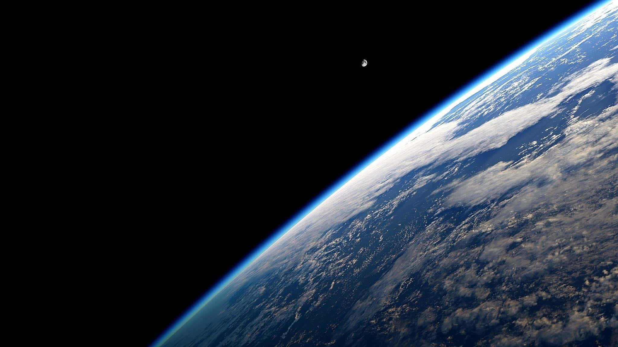 1440p 桌布 壁紙 — 地球在太空中雄偉地彎曲，帶有薄薄的藍色大氣層和旋轉的白雲，襯托著黑色的虛空，附近有一顆小月亮。