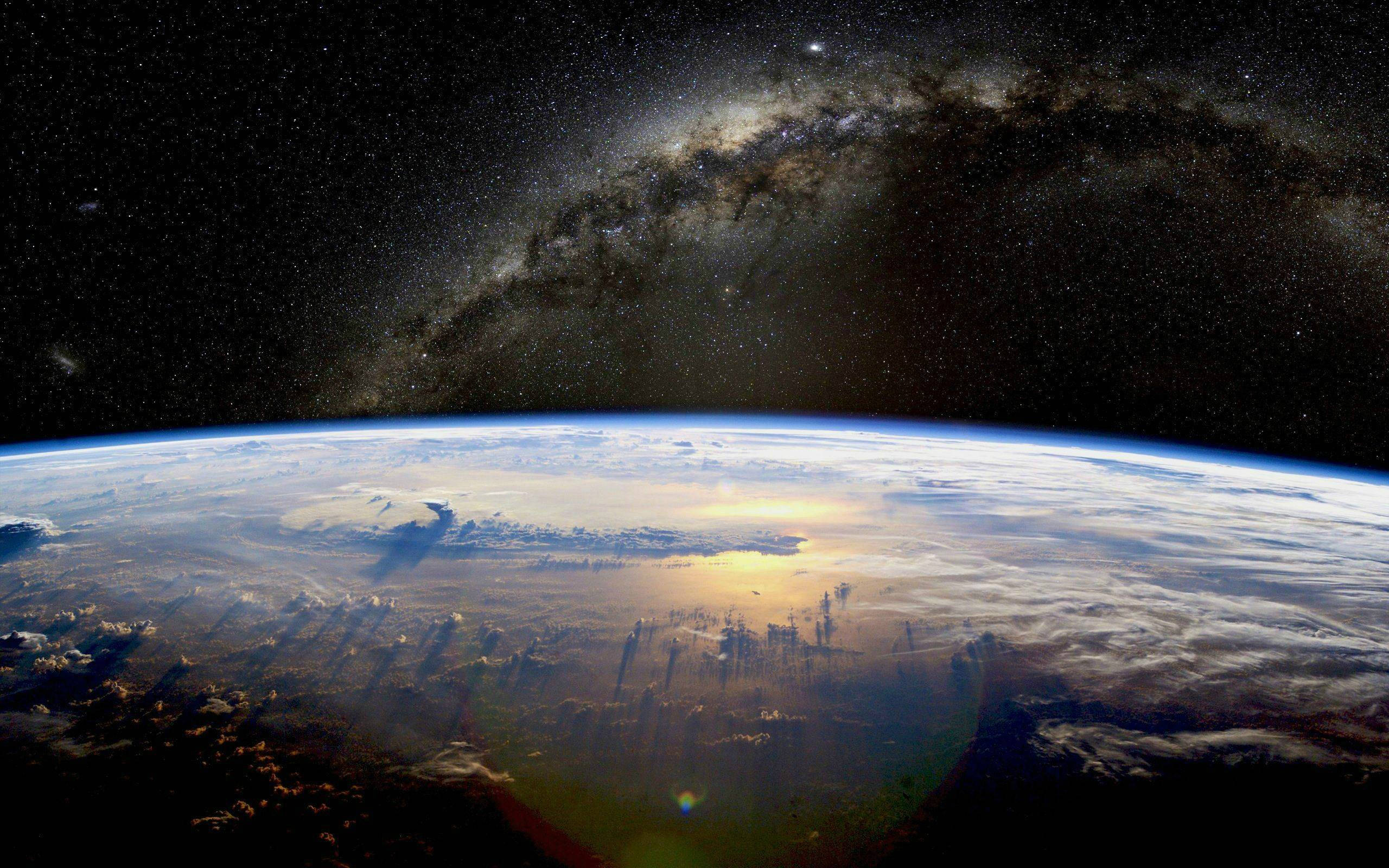 宇宙 桌布 壁紙 — 地球在星空下彎曲，銀河在頭頂拱起，陽光在雲層上閃爍。