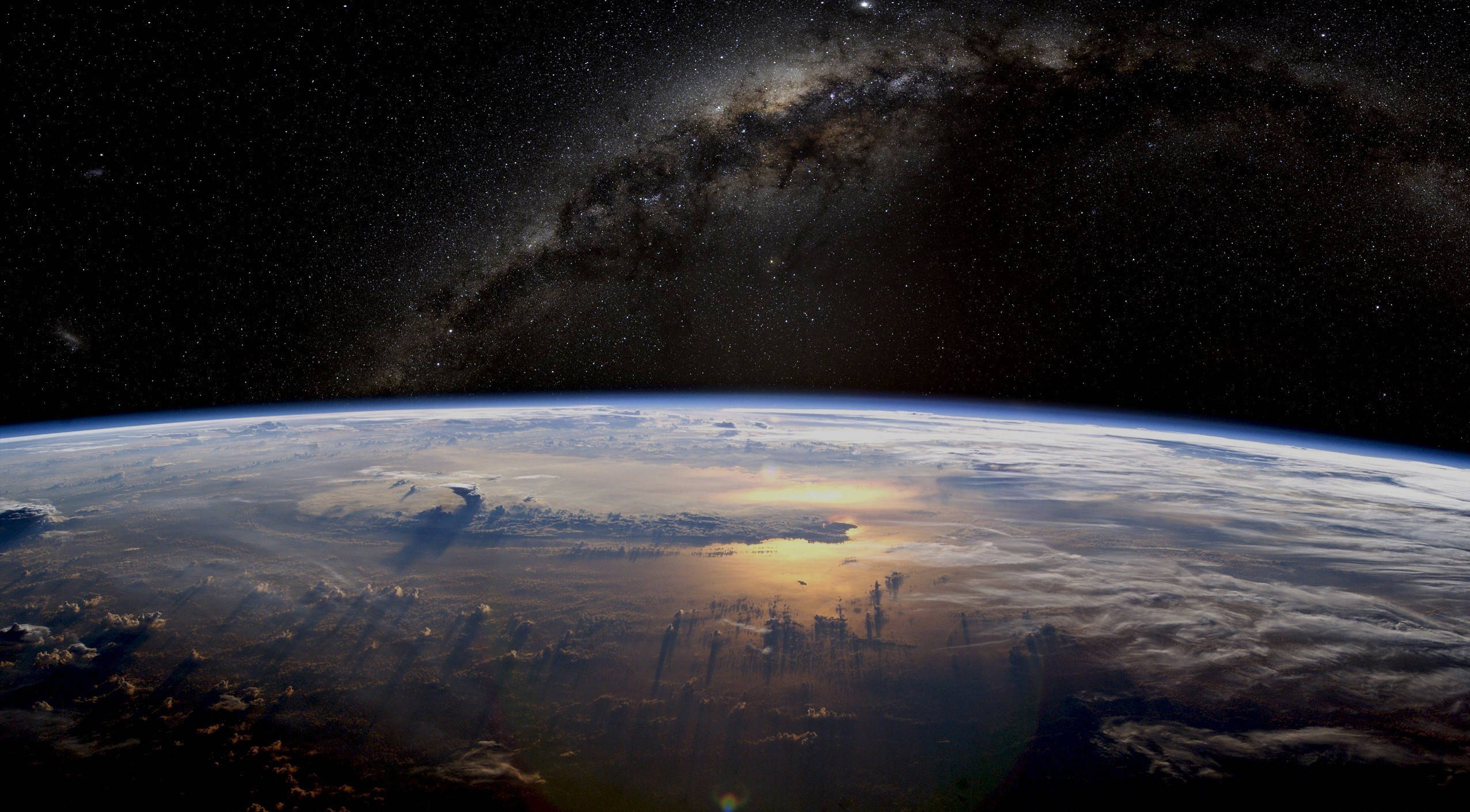 太空 桌布 壁紙 — 地球在星空下彎曲，銀河拱起，陽光在雲層上閃爍。