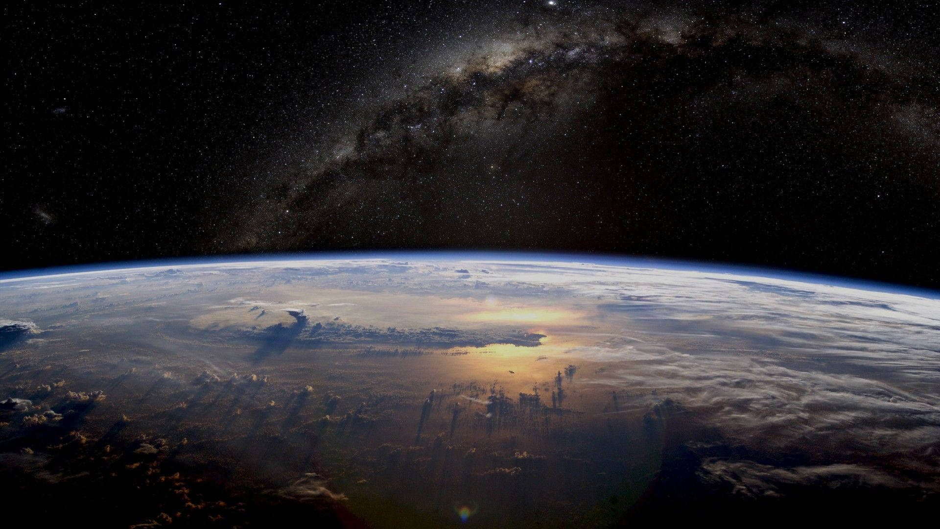 銀河 桌布 壁紙 — 地球在星空下彎曲，銀河拱起，陽光在雲層上閃爍。