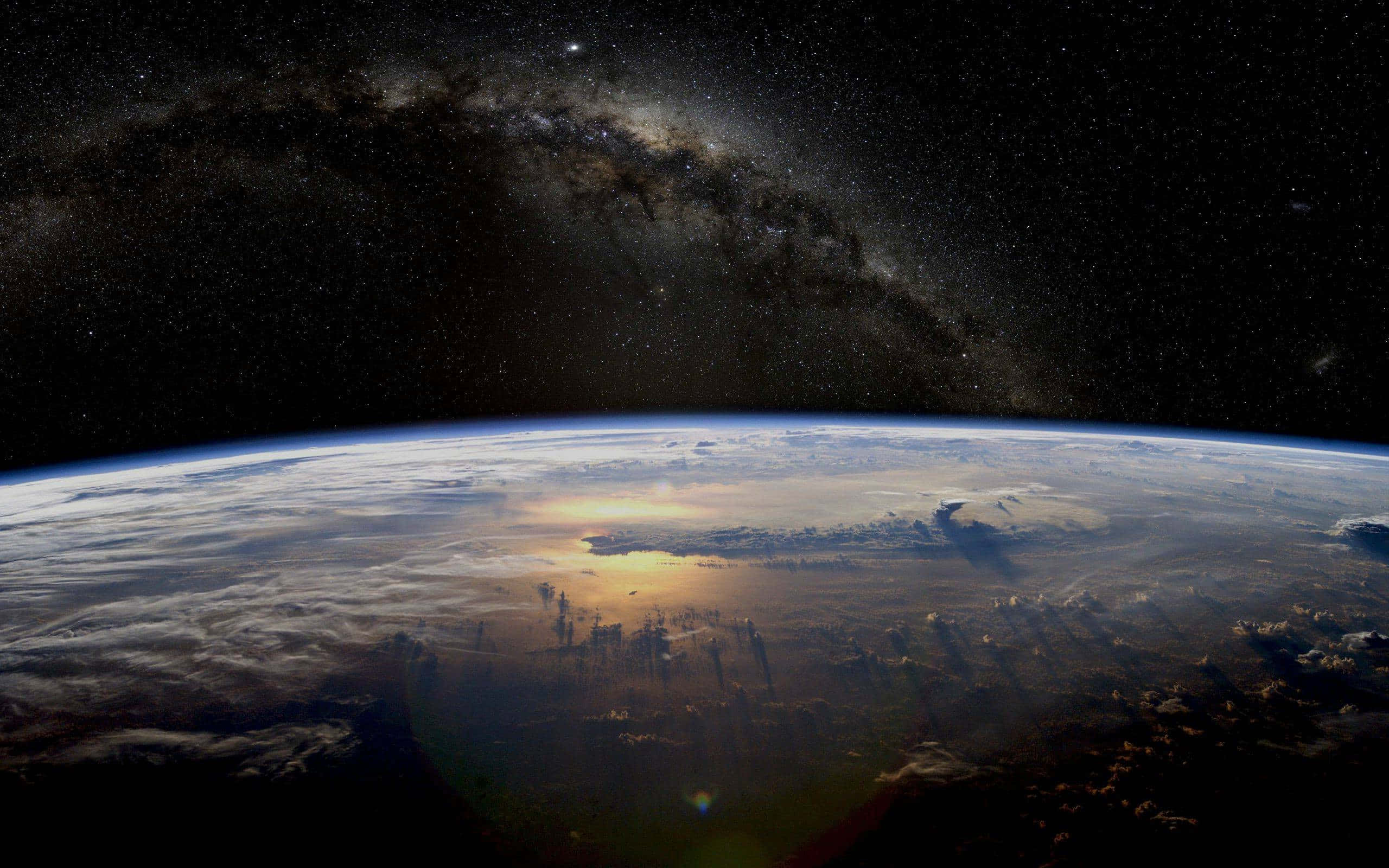 Real Space 桌布 壁紙 — 地球在星空下彎曲，銀河系在頭頂拱起，陽光在雲層上閃爍。