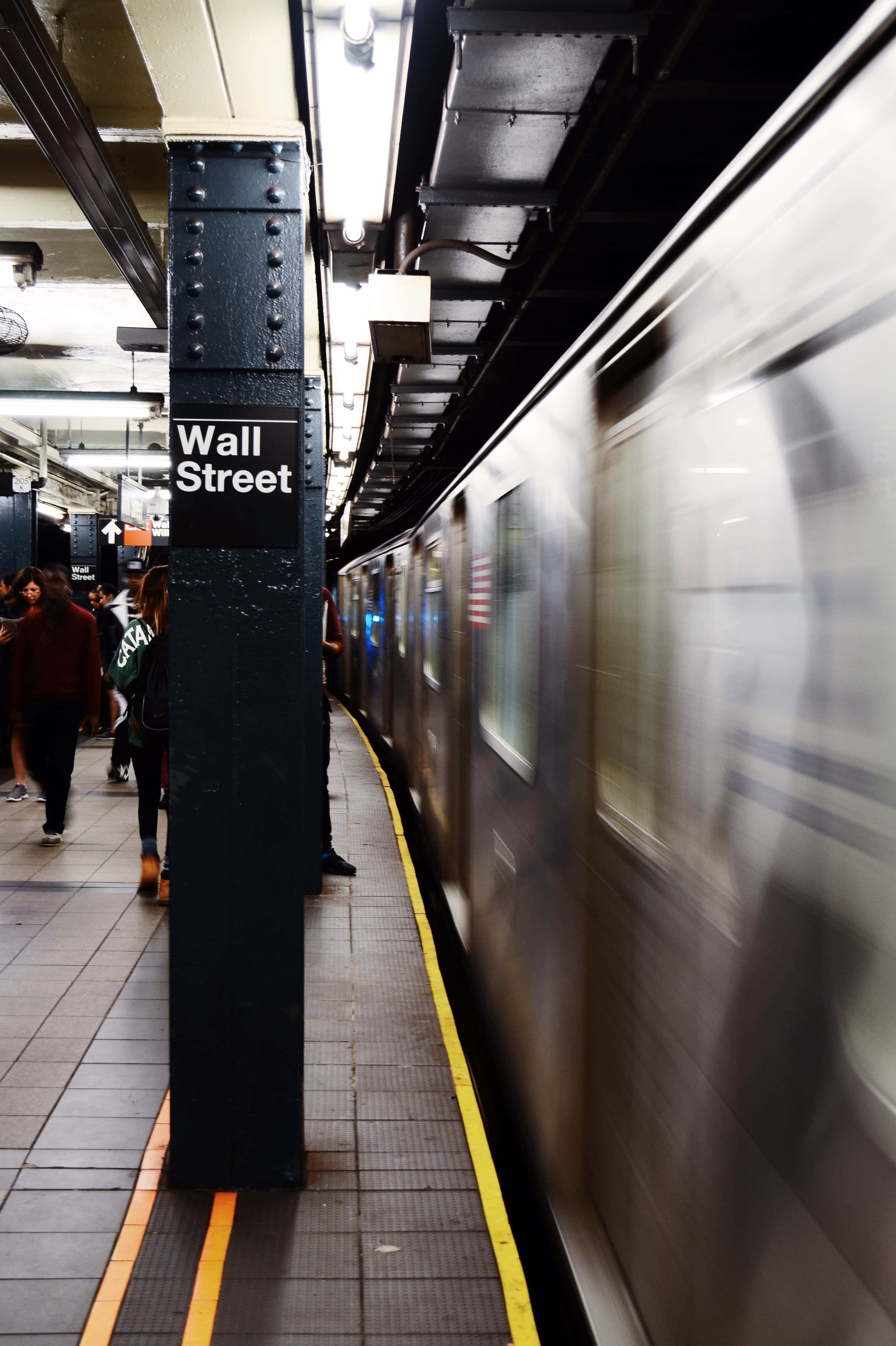 Wall Street 桌布 壁紙 — 地鐵列車模糊地駛過華爾街月台，通勤者在螢光燈下等候。