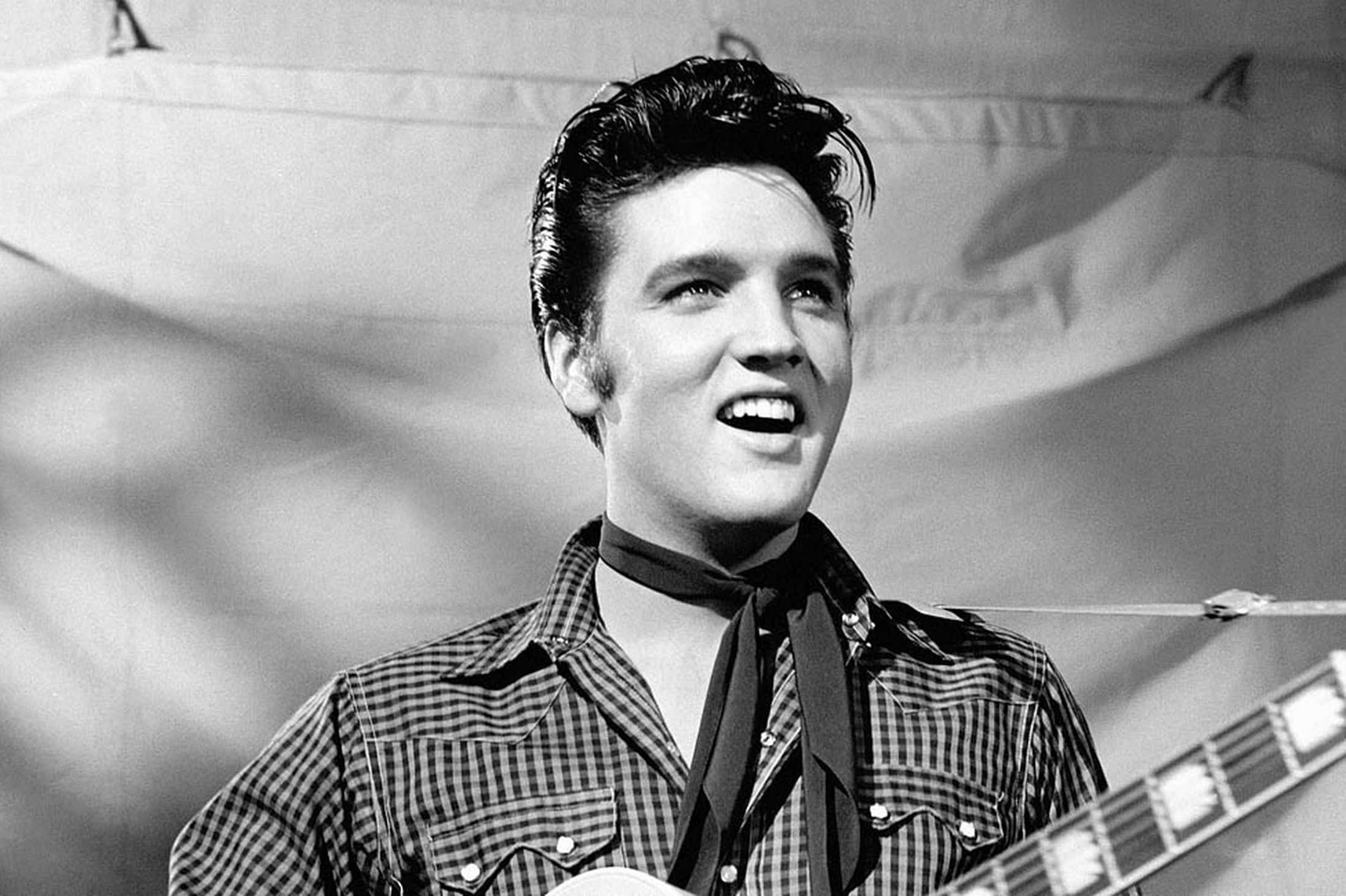 Elvis 桌布 壁紙 — 埃爾維斯·普雷斯利在一張有布簾背景的黑白照片中，燦爛地笑著拿著吉他。