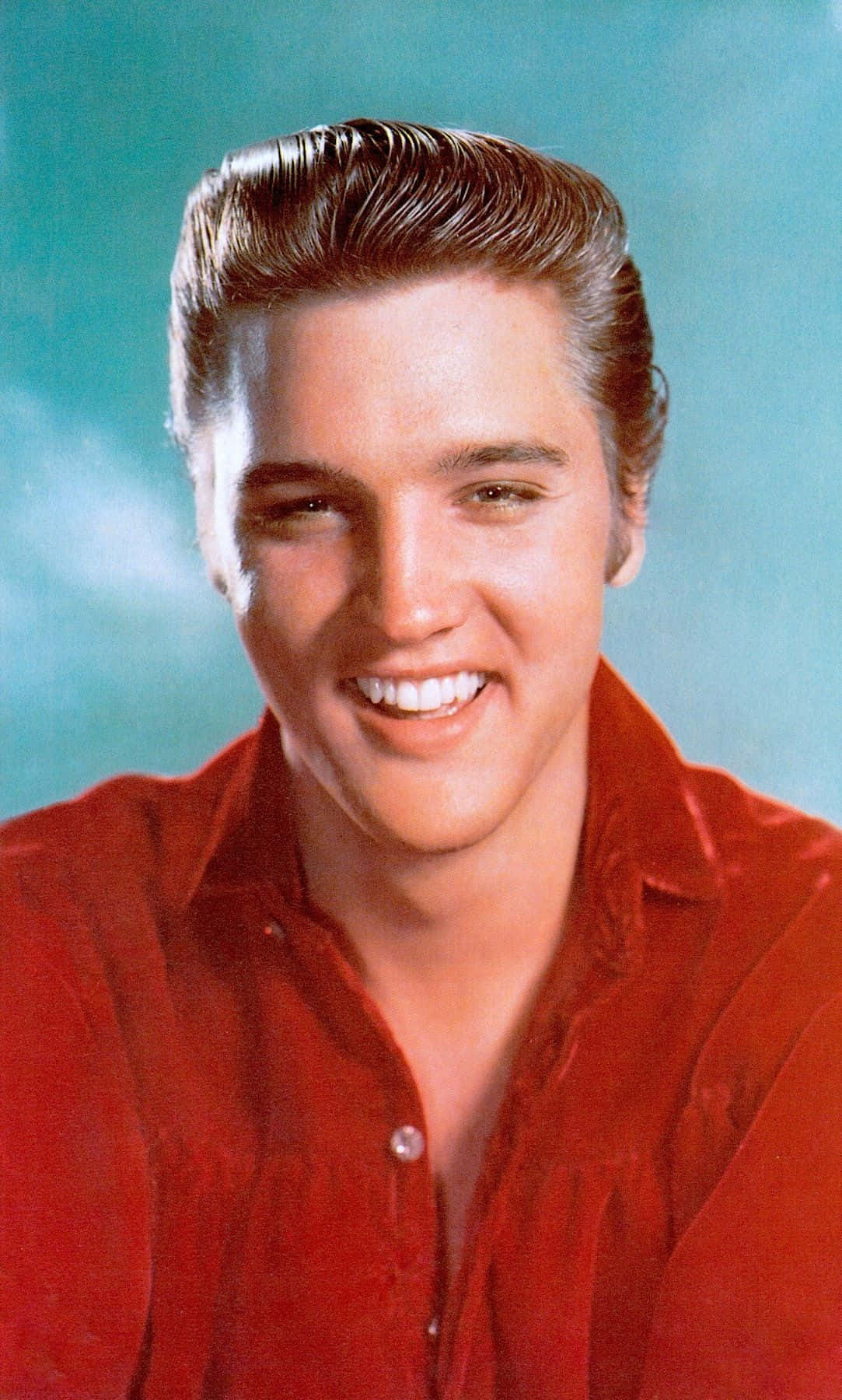 Elvis 桌布 壁紙 — 埃爾維斯·普雷斯利穿著紅色襯衫，在青綠色攝影棚背景下，以經典1950年代髮型燦爛微笑。
