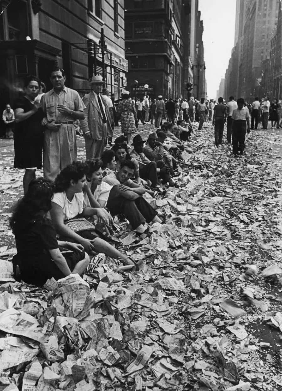 history 桌布 壁紙 — 城市中一條佈滿報紙碎片的街道上，人們坐著和站著的黑白照片。