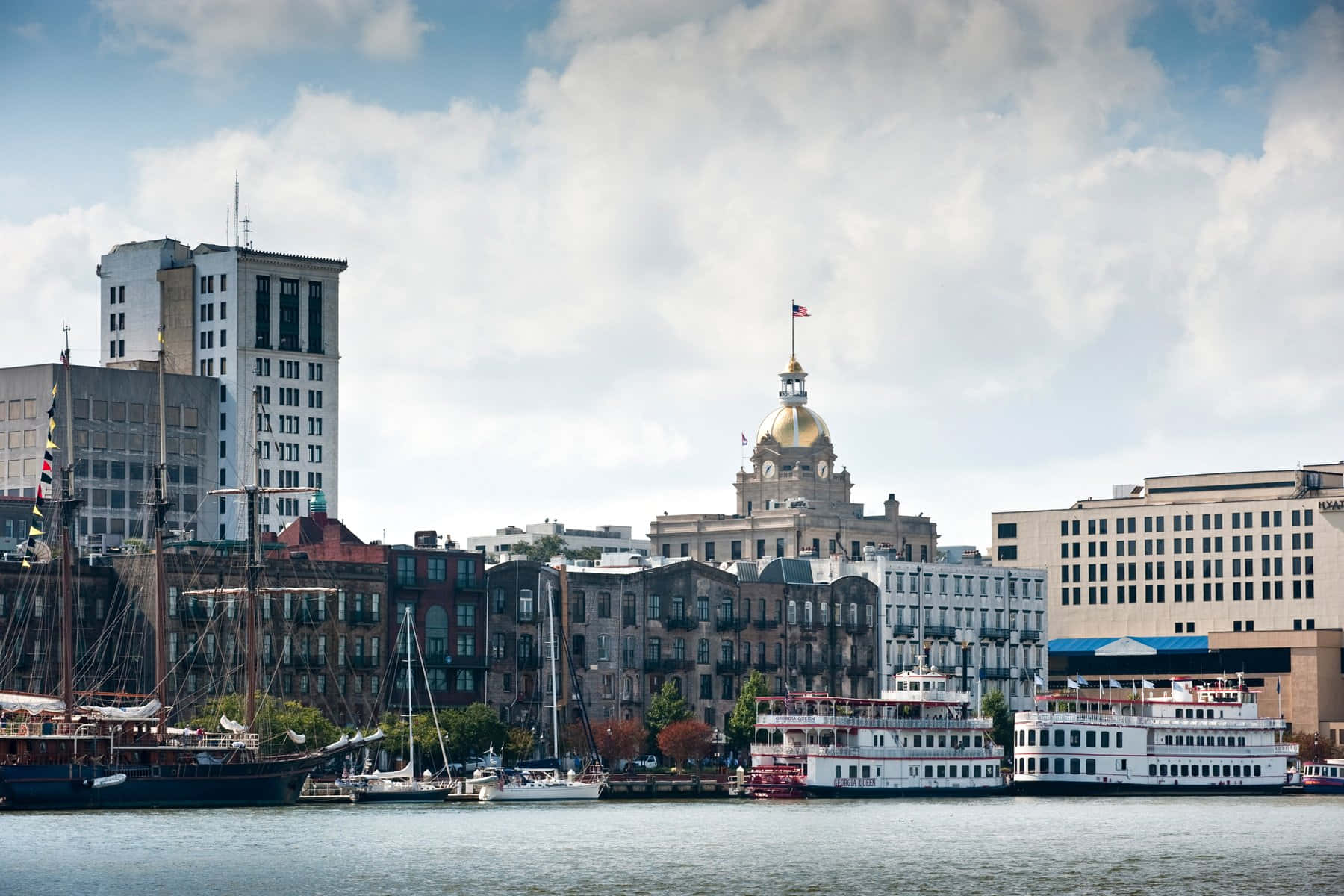 Savannah 桌布 壁紙 — 城市天際線，歷史建築和船隻停泊在河邊，天空部分多雲。