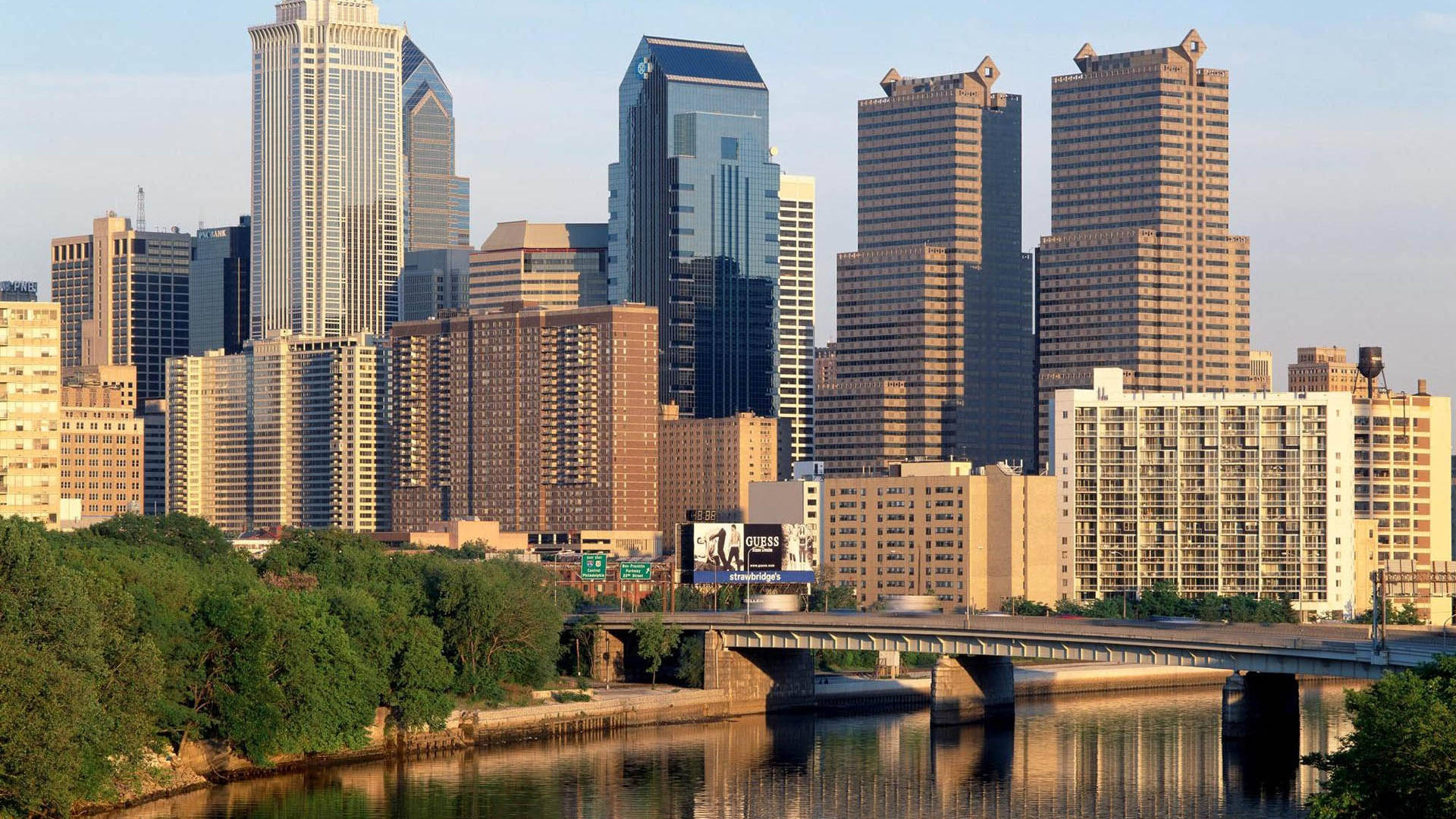 Philadelphia 桌布 壁紙 — 城市天際線，高聳的玻璃和混凝土摩天大樓倒映在平靜的河面上，天空清澈湛藍。