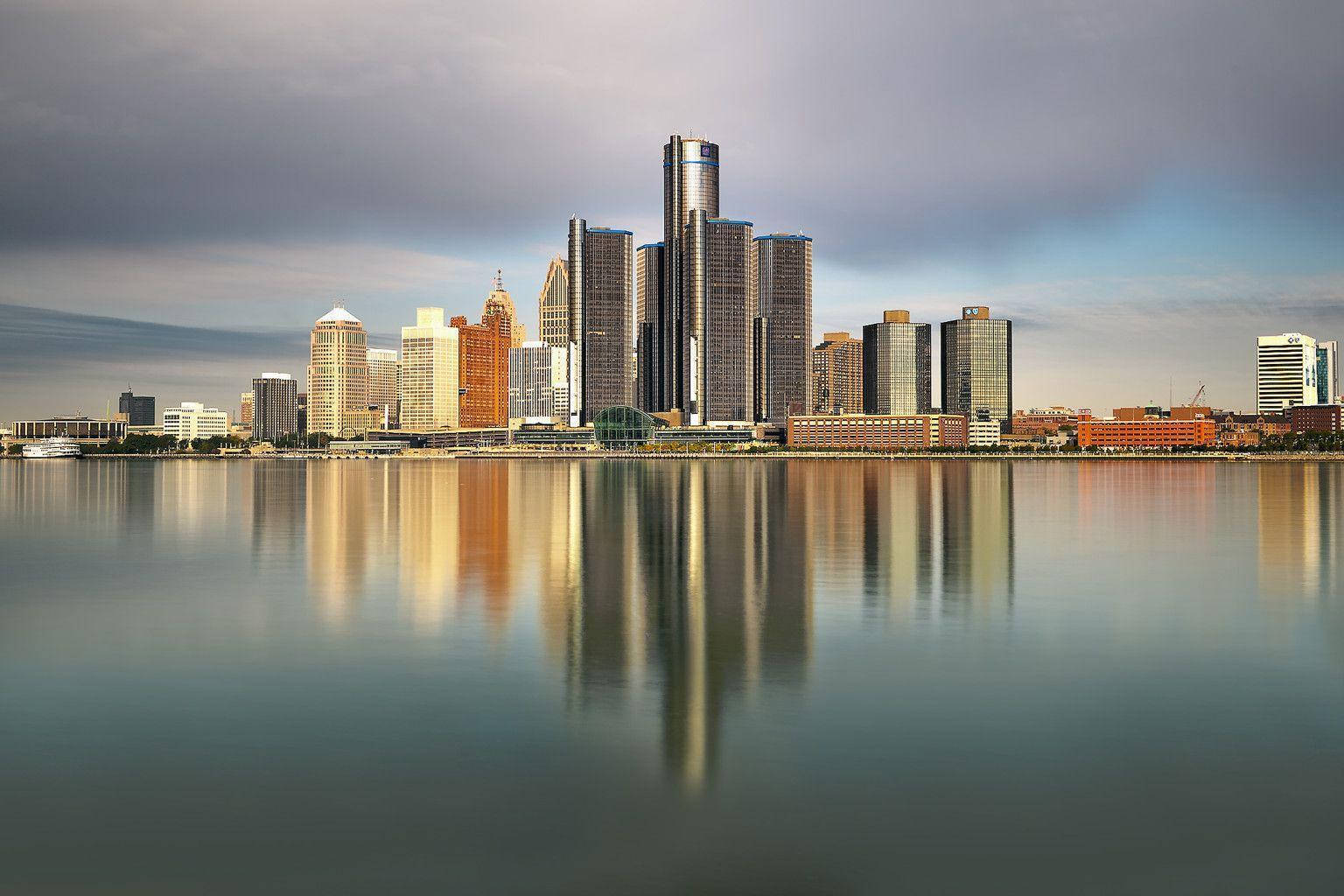 detroit 桌布 壁紙 — 城市天際線，高聳的玻璃摩天大樓在多雲的天空下完美倒映在平靜的水面上。