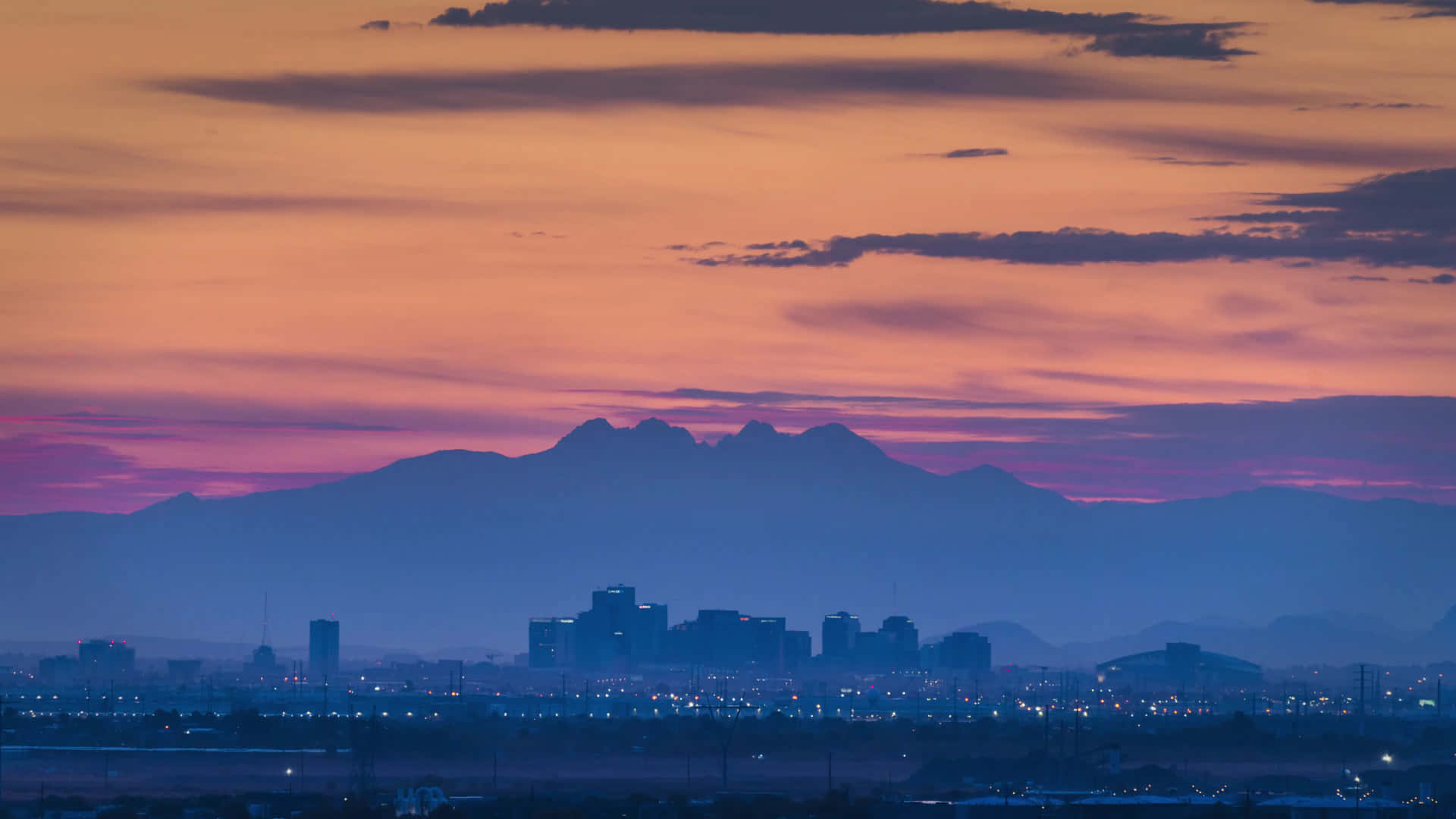 Phoenix Arizona 桌布 壁紙 — 城市天際線在充滿活力的橙色和紫色日落映襯下形成剪影，背景有遠處的山脈。