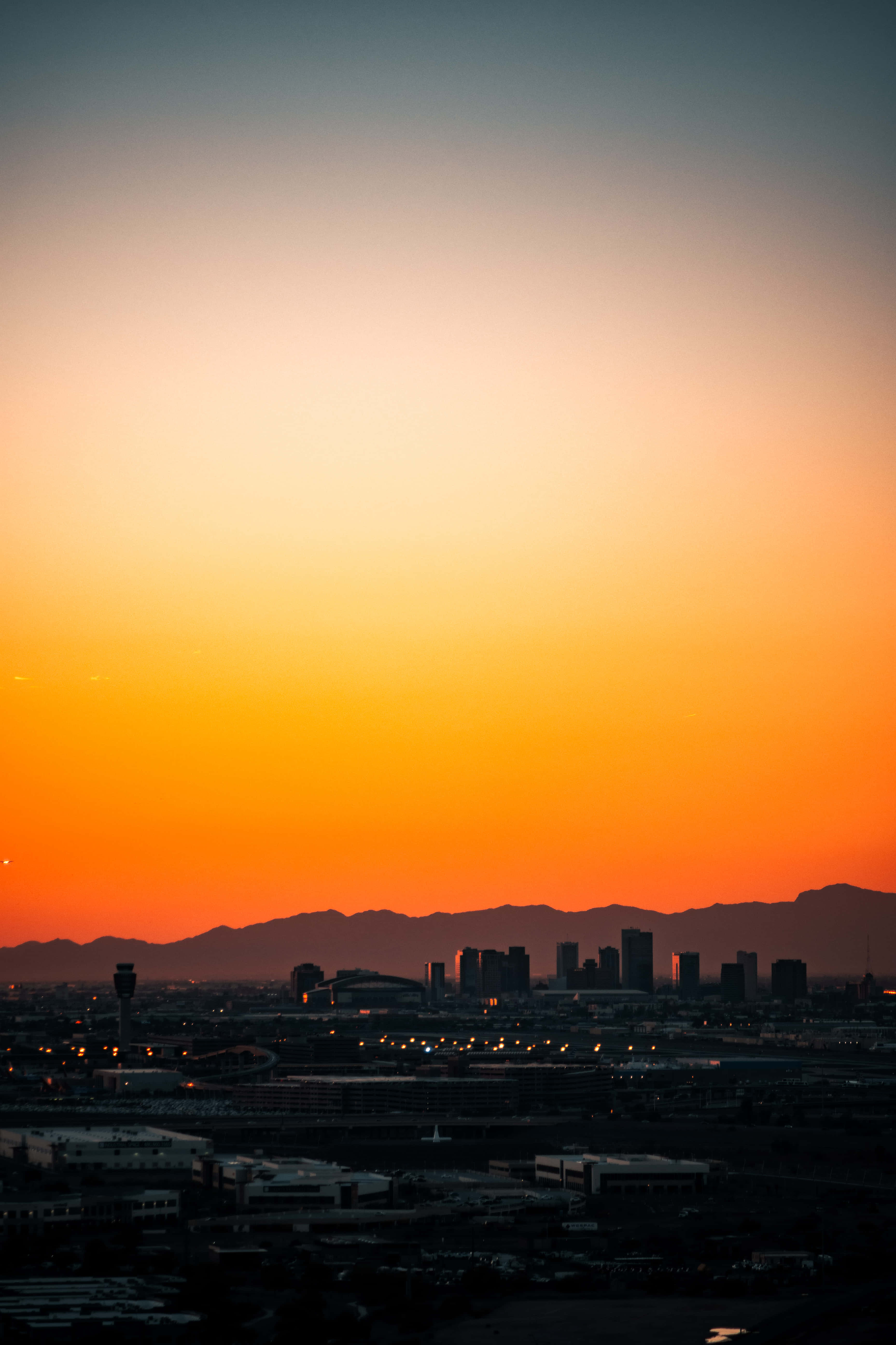 Phoenix Arizona 桌布 壁紙 — 城市天際線在充滿活力的橙色和藍色日落天空下形成剪影，遠方有山脈。