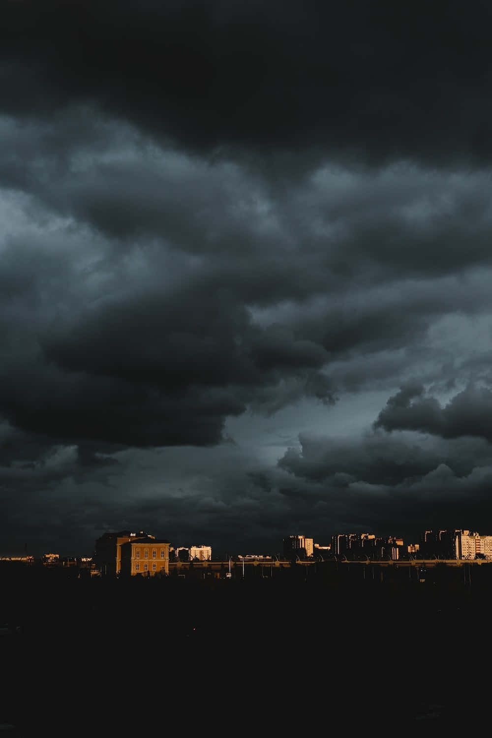 Dark Sky 桌布 壁紙 — 城市天際線在廣闊而陰沉、佈滿厚重烏雲的天空下呈現剪影。