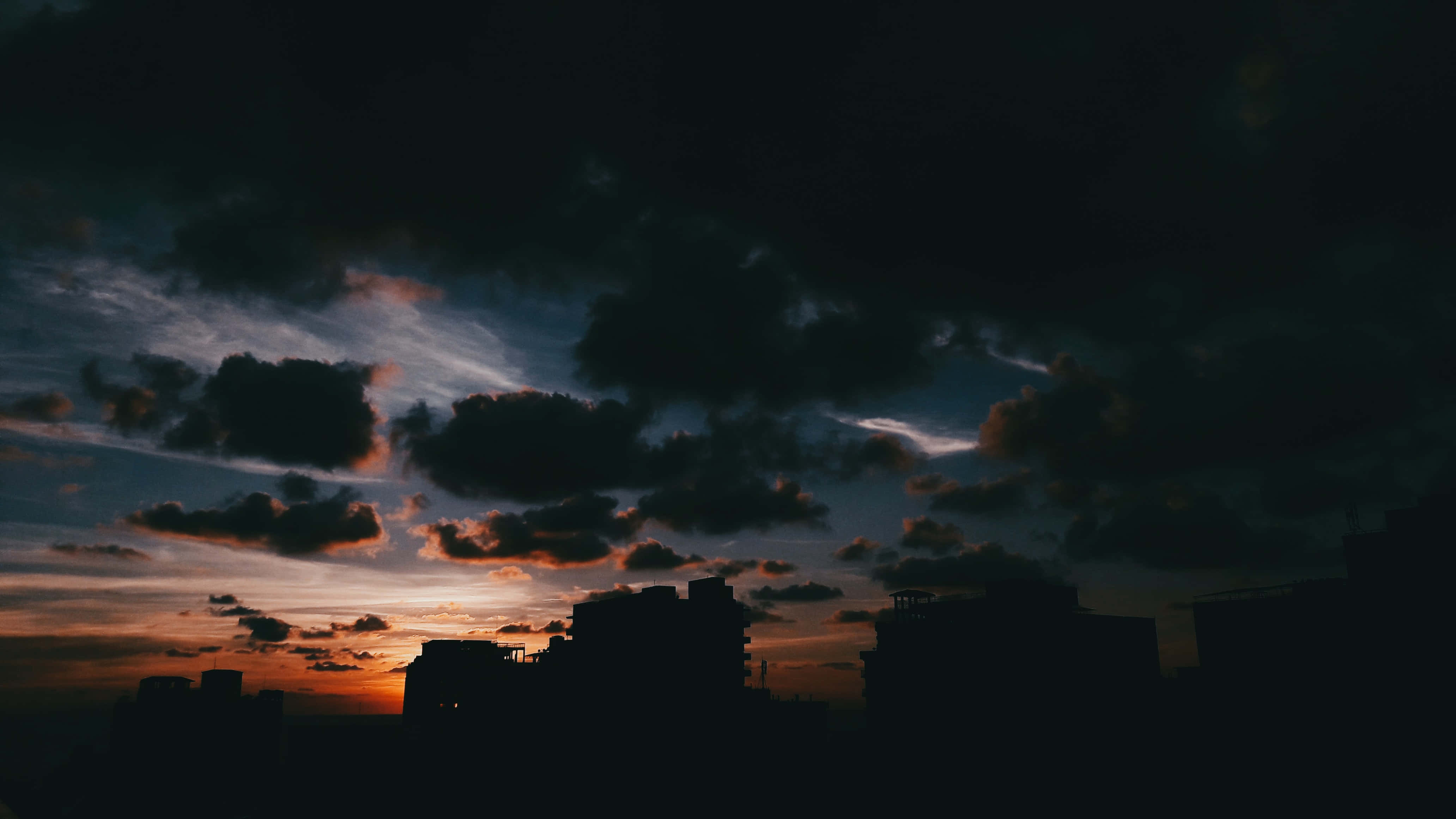 Dark Sky 桌布 壁紙 — 城市天際線在戲劇性的暮色天空下形成剪影，天空中有火紅的橙色雲朵和深藍色的陰影。