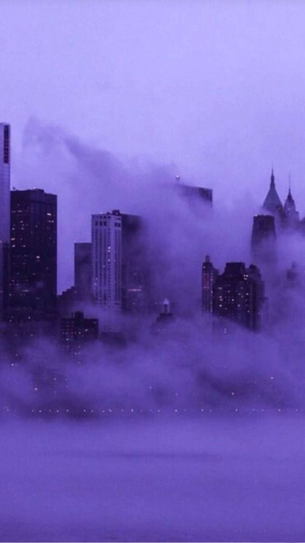 雲朵 桌布 壁紙 — 城市天際線從濃密的紫色霧氣中浮現，發光的窗戶穿透迷濛的大氣。