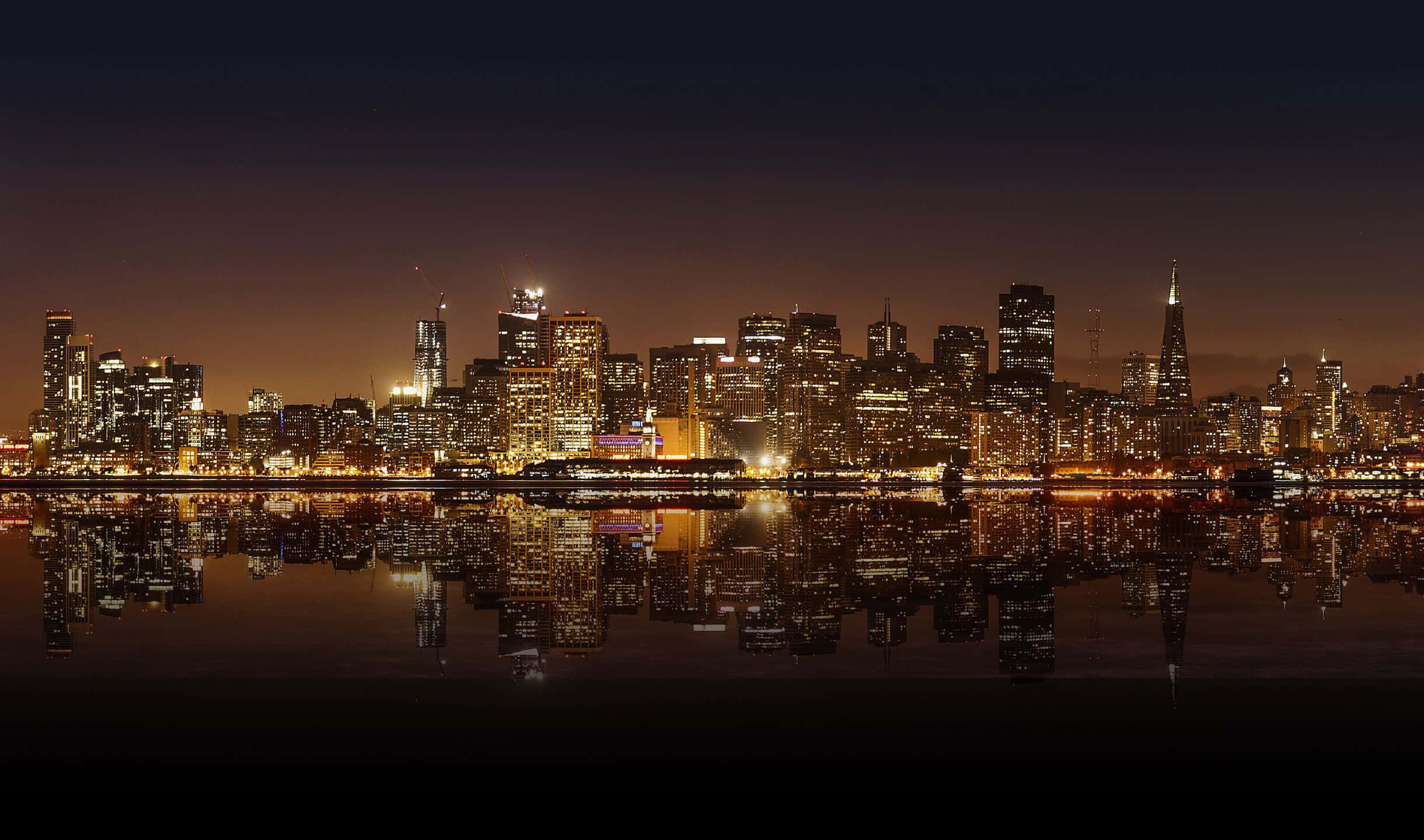 2440x1440 San Francisco 桌布 壁紙 — 城市天際線的 panoramic 夜景，發光的摩天大樓完美倒映在平靜的水面上。