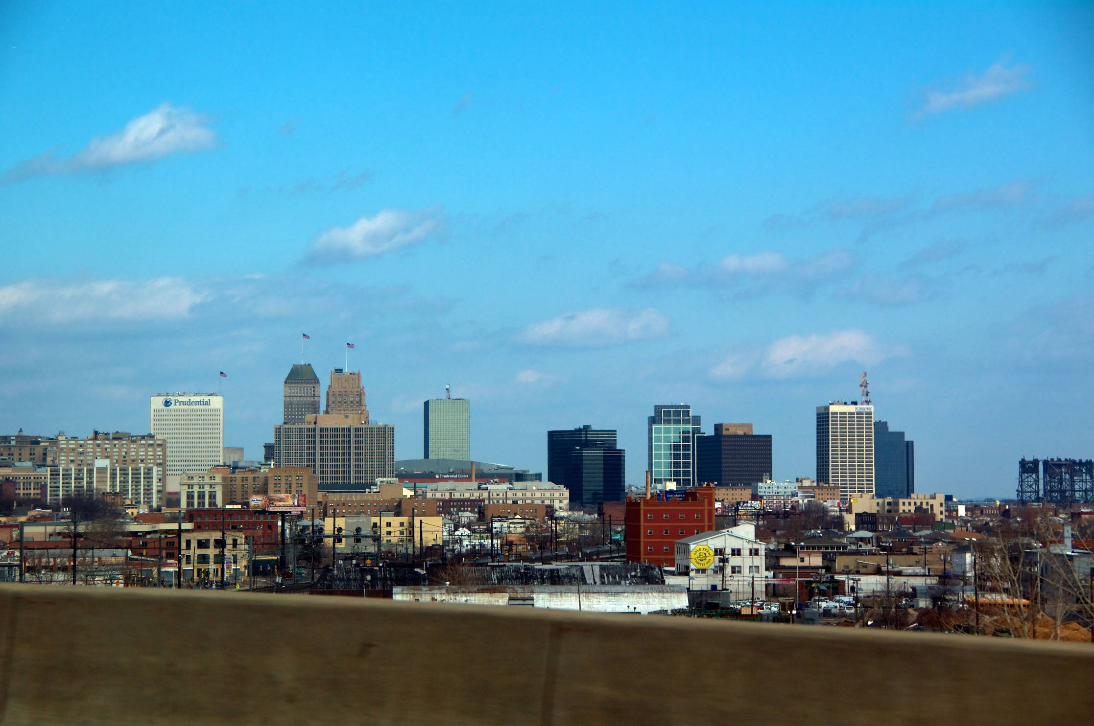 New Jersey 桌布 壁紙 — 城市天際線的全景視圖，現代摩天大樓和歷史建築在明亮的藍天白雲下。