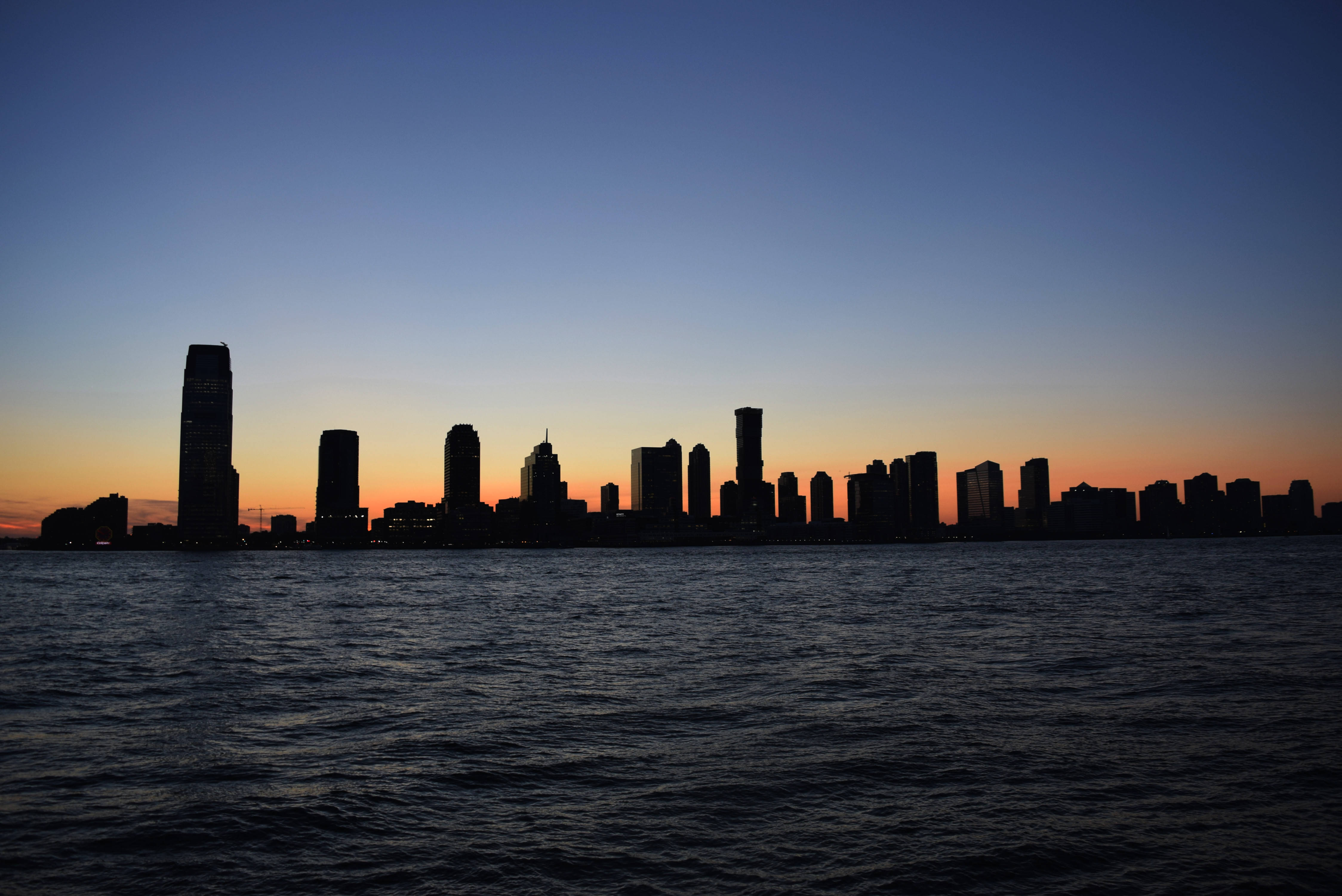 Nyc 桌布 壁紙 — 城市天際線的摩天大樓剪影在漣漪水面上方漸變的日落天空中升起。