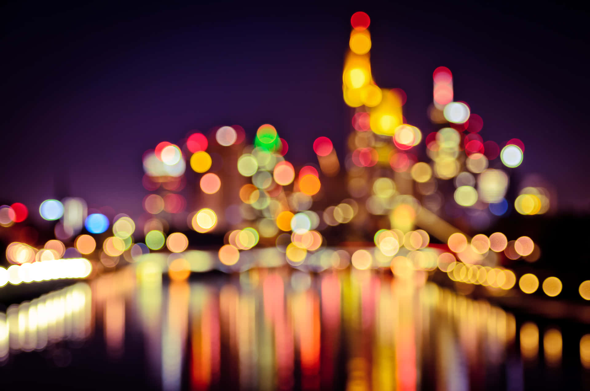 Bokeh 桌布 壁紙 — 城市天際線的散景燈光在夜間在水面上閃爍，帶有溫暖發光的倒影。