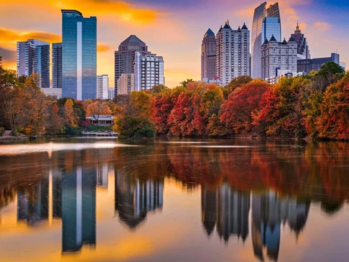 Atlanta Georgia 桌布 壁紙 — 城市天際線與玻璃摩天大樓在平靜的湖面上倒映，周圍環繞著充滿活力的秋葉，在溫暖的日落天空下。