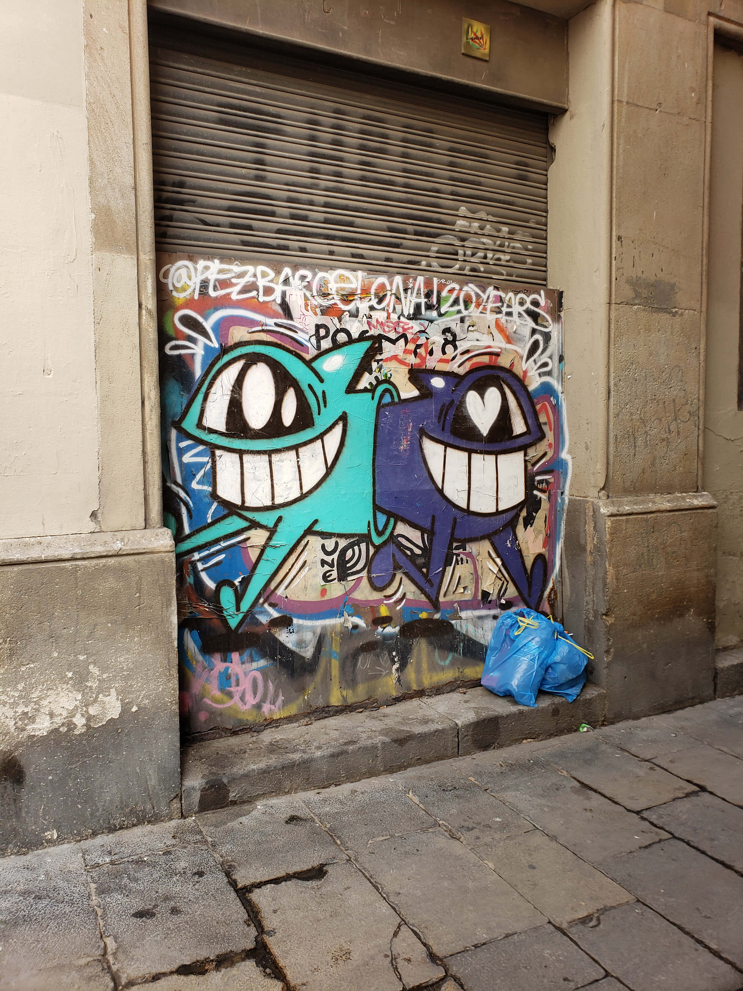 Graffiti Art 桌布 壁紙 — 城市小巷中關閉的金屬百葉窗上繪有兩個大眼睛微笑角色的鮮豔卡通塗鴉。