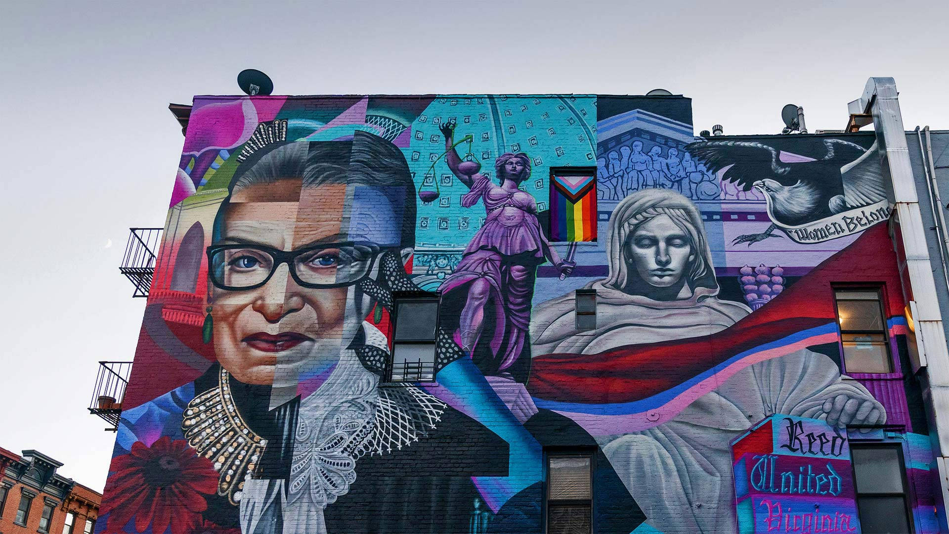 Ruth Bader Ginsburg 桌布 壁紙 — 城市建築物上充滿活力的壁畫，描繪了露絲·巴德·金斯伯格、正義女神和一位手持「Women Belong」橫幅的女性。