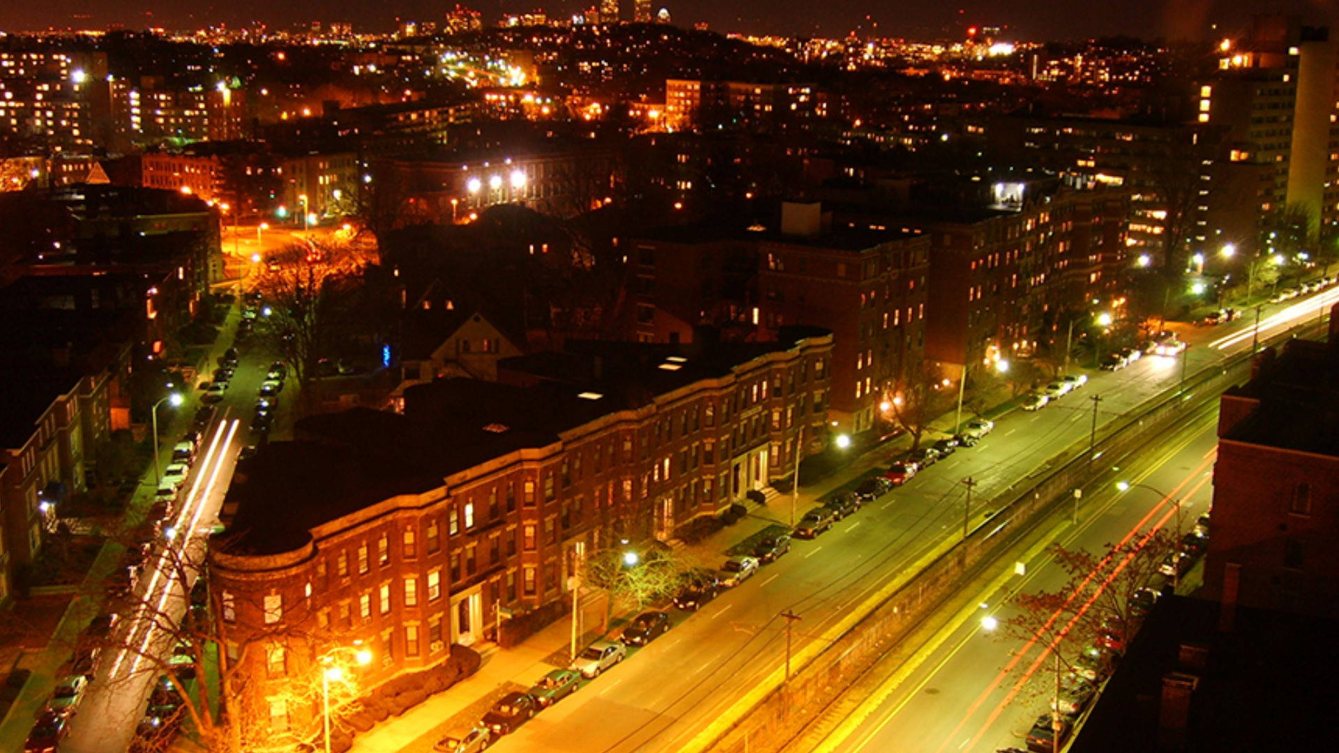 Massachusetts 桌布 壁紙 — 城市景觀的夜間鳥瞰圖，發光的街燈和流動的車燈照亮了磚砌建築和道路。