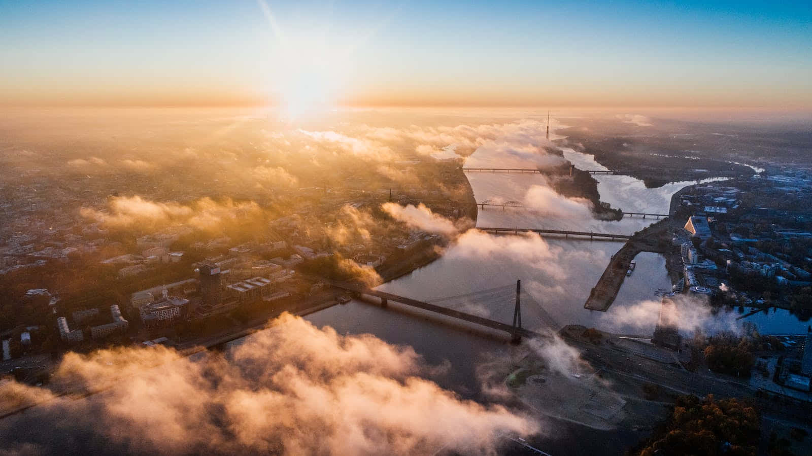 Cute Sunset 桌布 壁紙 — 城市河流的鳥瞰圖，橋樑穿過金色晨霧，太陽從地平線升起。