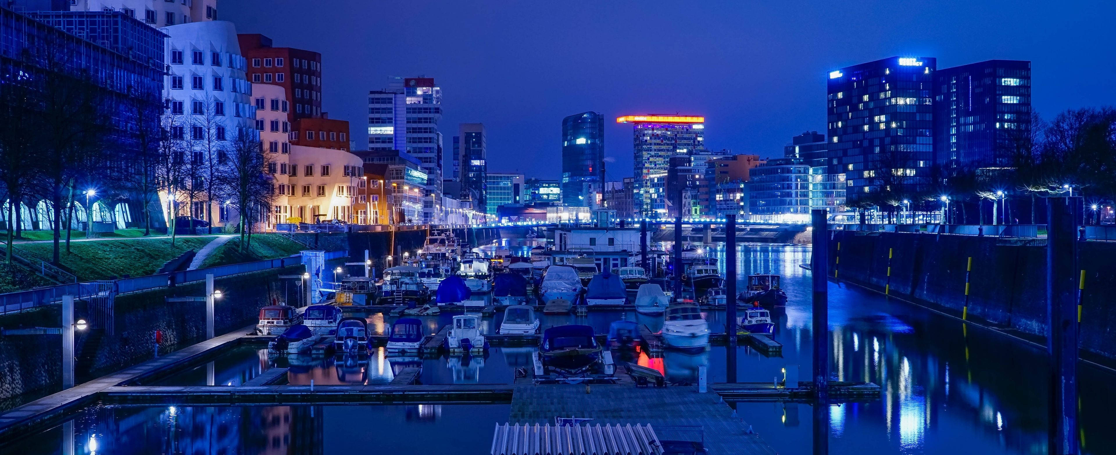 3840x1600 桌布 壁紙 — 城市運河的寧靜夜景，停泊的船隻倒映著現代建築的霓虹燈光。