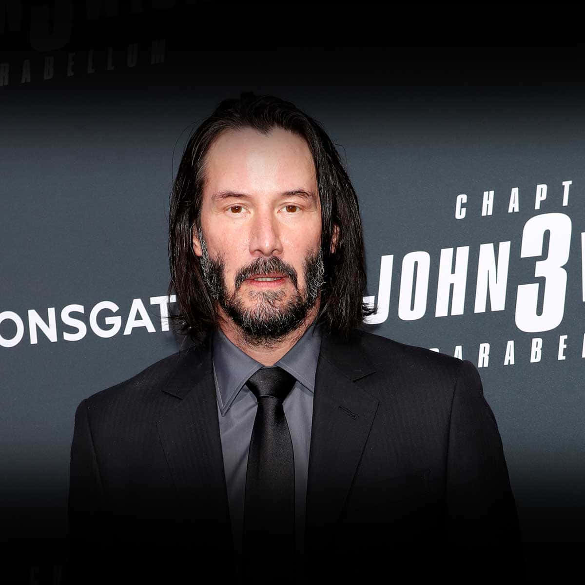 基努·李維 桌布 壁紙 — 基努·李維身穿黑色西裝，站在帶有『John Wick Chapter 3』文字的深色背景前。