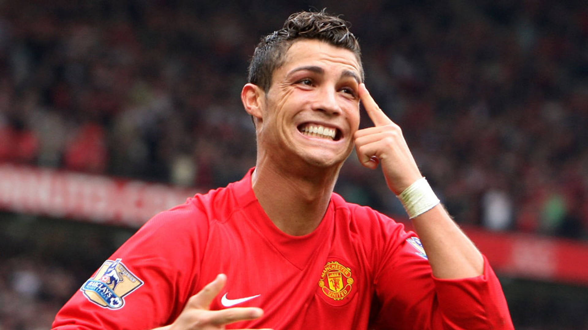 Ronaldo 桌布 壁紙 — 基斯坦奴·朗拿度身穿紅色曼聯球衣，在球場人群中咧嘴大笑，同時指向自己的太陽穴。