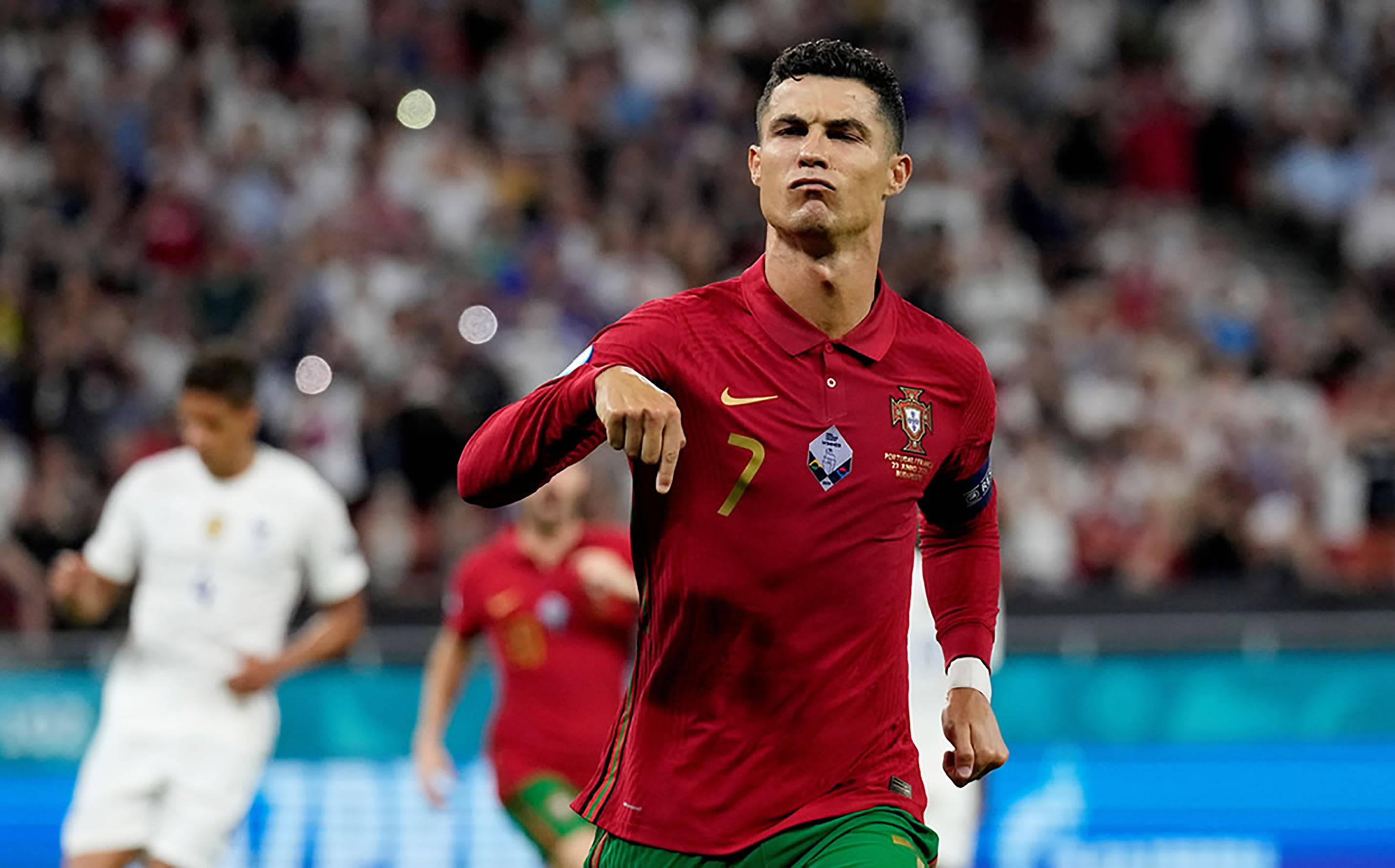 Ronaldo 桌布 壁紙 — 基斯坦奴·朗拿度身穿紅色葡萄牙球衣，在足球比賽中自信地指向某處，背景是模糊的球場觀眾。