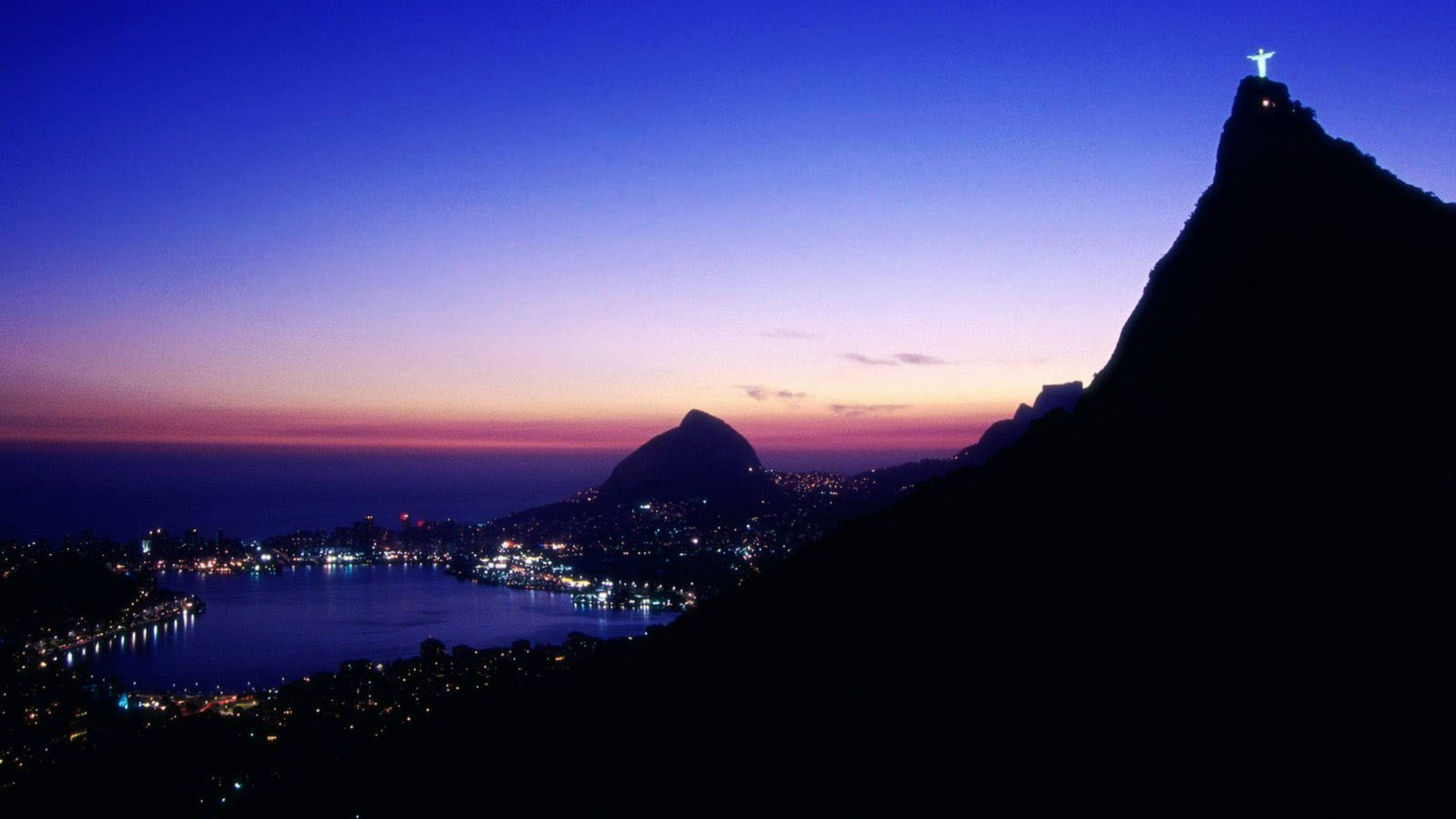 rio 桌布 壁紙 — 基督像在科爾科瓦多山頂發光，里約熱內盧的城市燈光在暮色中閃爍。