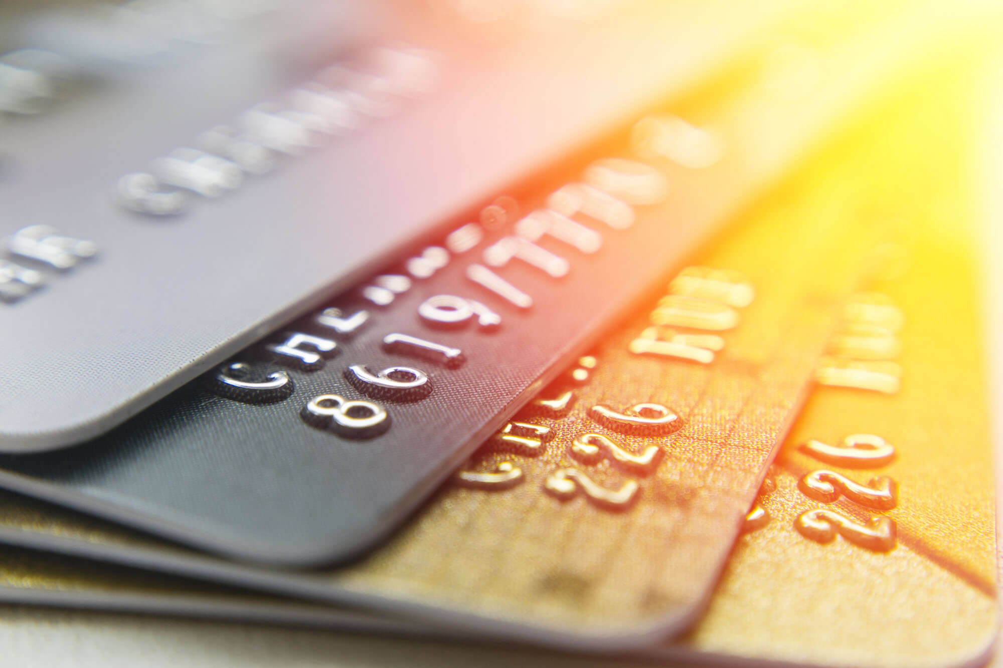 Credit Card 桌布 壁紙 — 堆疊信用卡的特寫，溫暖的鏡頭光暈突出金屬浮雕數字和標誌。