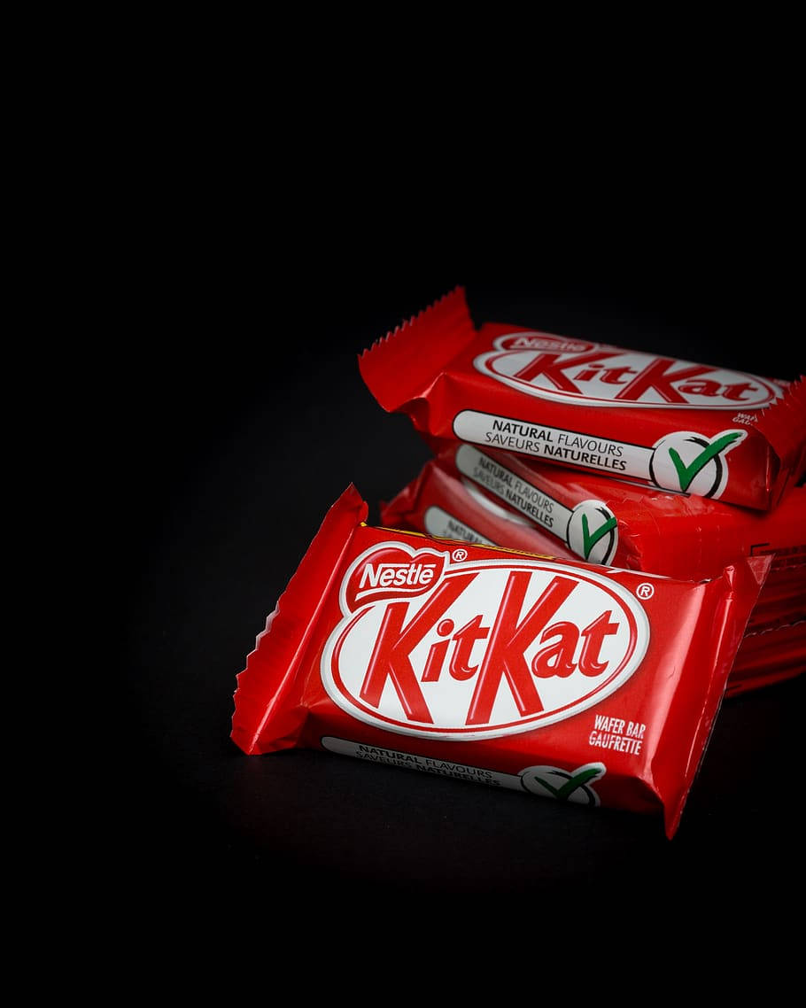 糖果 桌布 壁紙 — 堆疊的KitKat巧克力棒以鮮紅色包裝在攝影棚燈光下於純黑背景上閃閃發光。