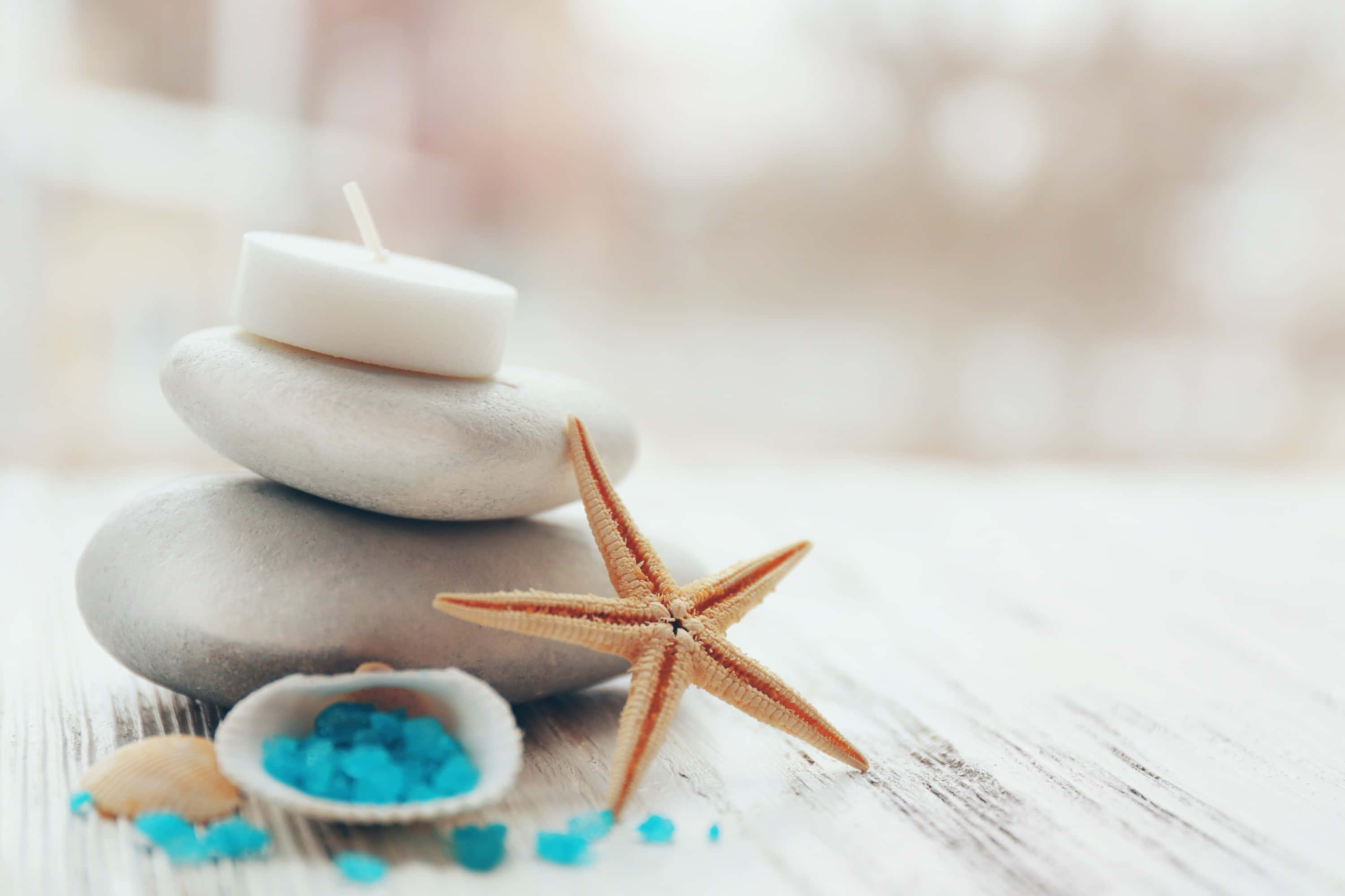 Spa Treatments 桌布 壁紙 — 堆疊的平滑灰色石頭在風化的木質表面上，旁邊有海星和藍色珠子，支撐著一支白色蠟燭。