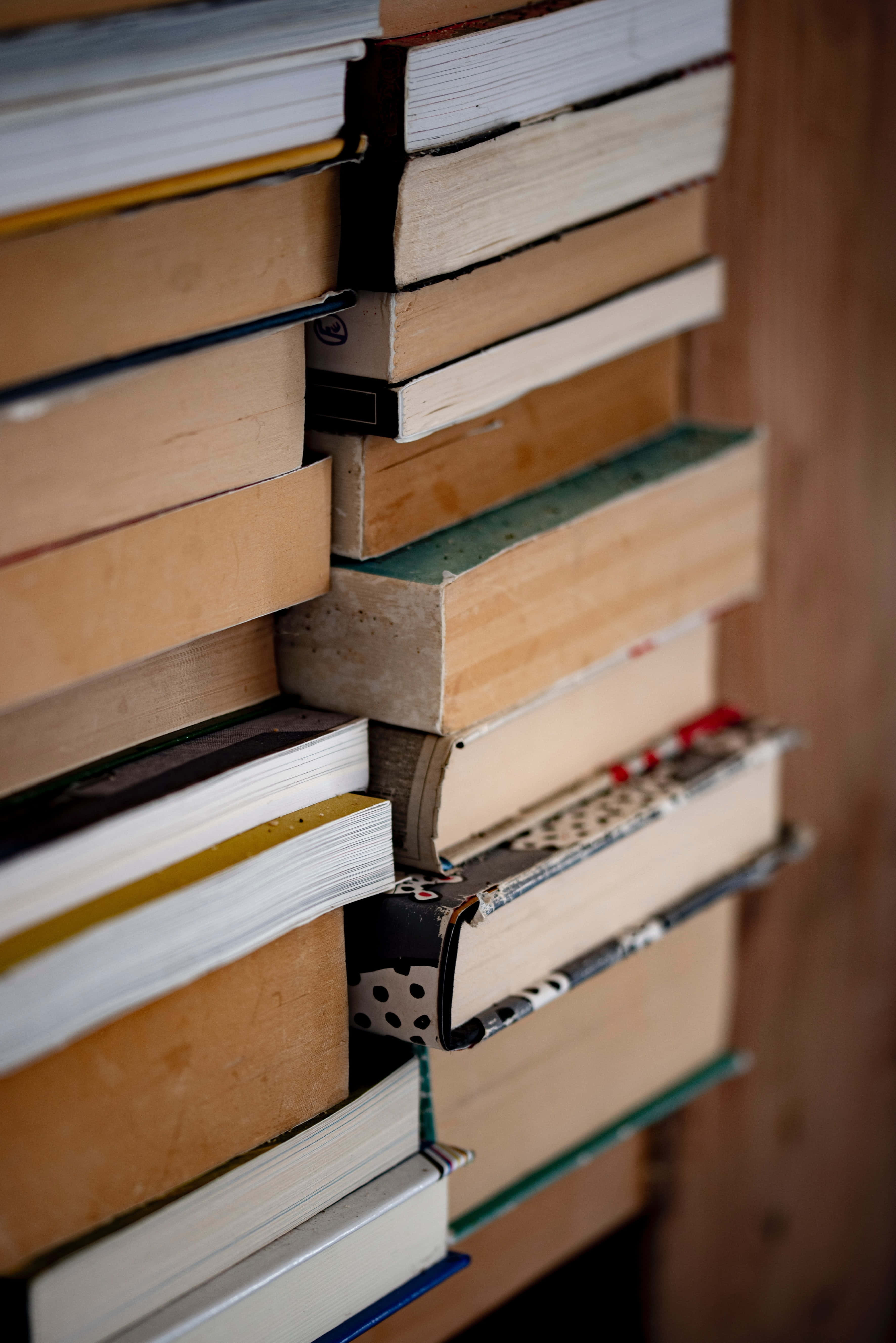 Books iPhone 桌布 壁紙 — 堆疊的書籍，書脊各異，邊緣磨損，在溫暖的自然光中營造出質感豐富的知識之牆。