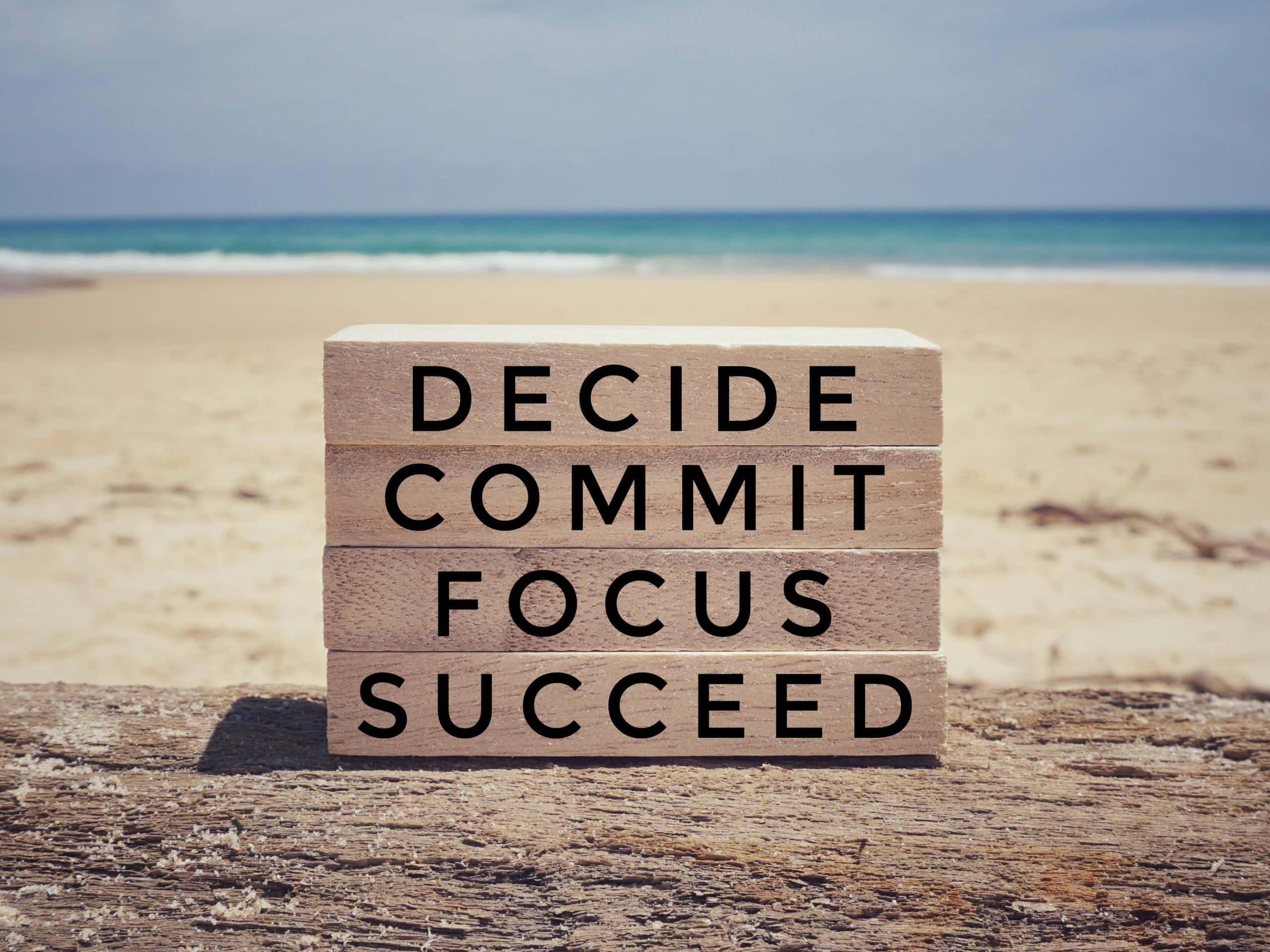2560x1920 桌布 壁紙 — 堆疊的木塊拼出「decide commit focus succeed」，放在陽光明媚的海灘浮木上，伴隨著海浪。