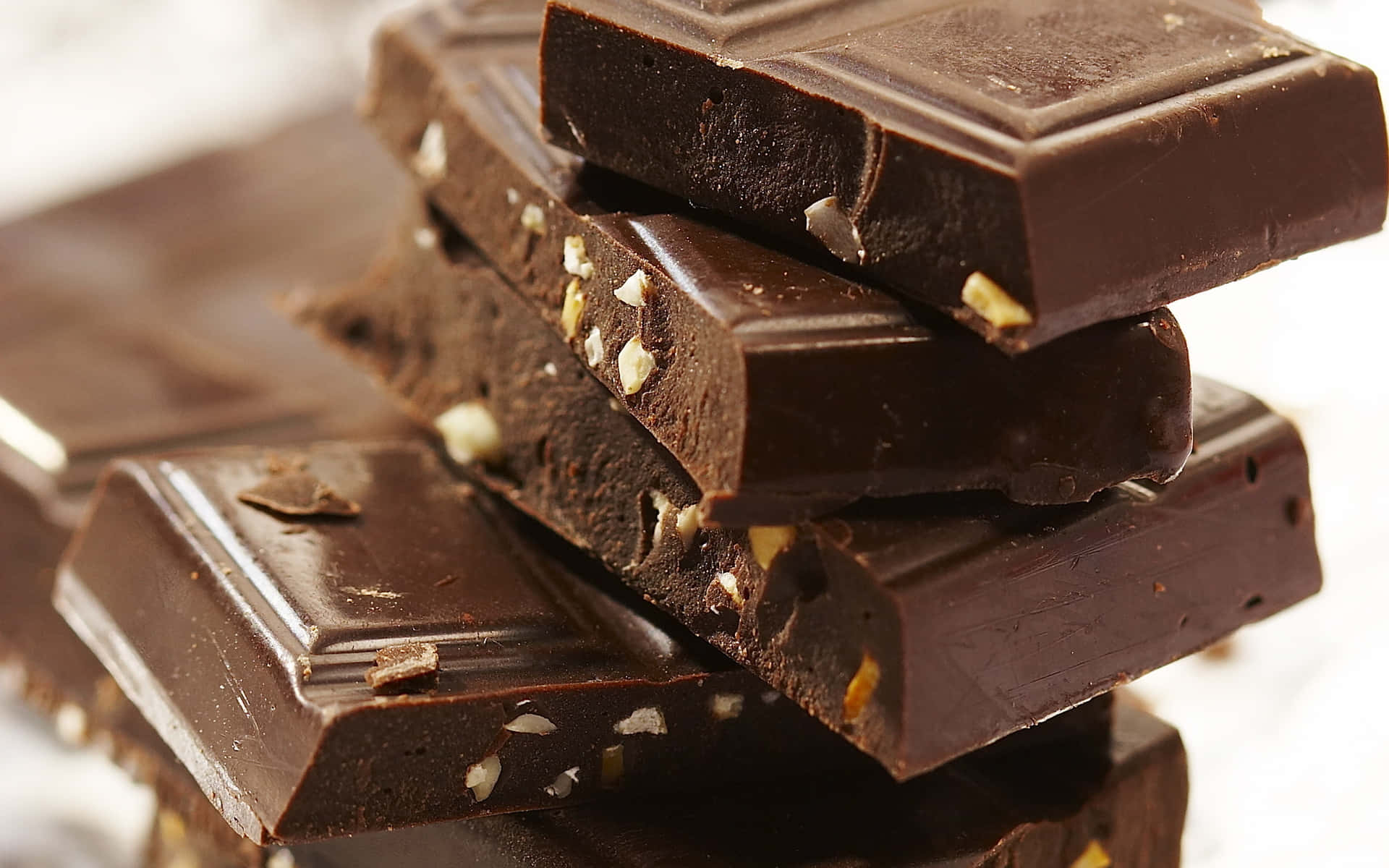 Brown Chocolate 桌布 壁紙 — 堆疊的深色巧克力條帶有可見的堅果碎片，在柔和光線下於亮白色背景上閃閃發光。
