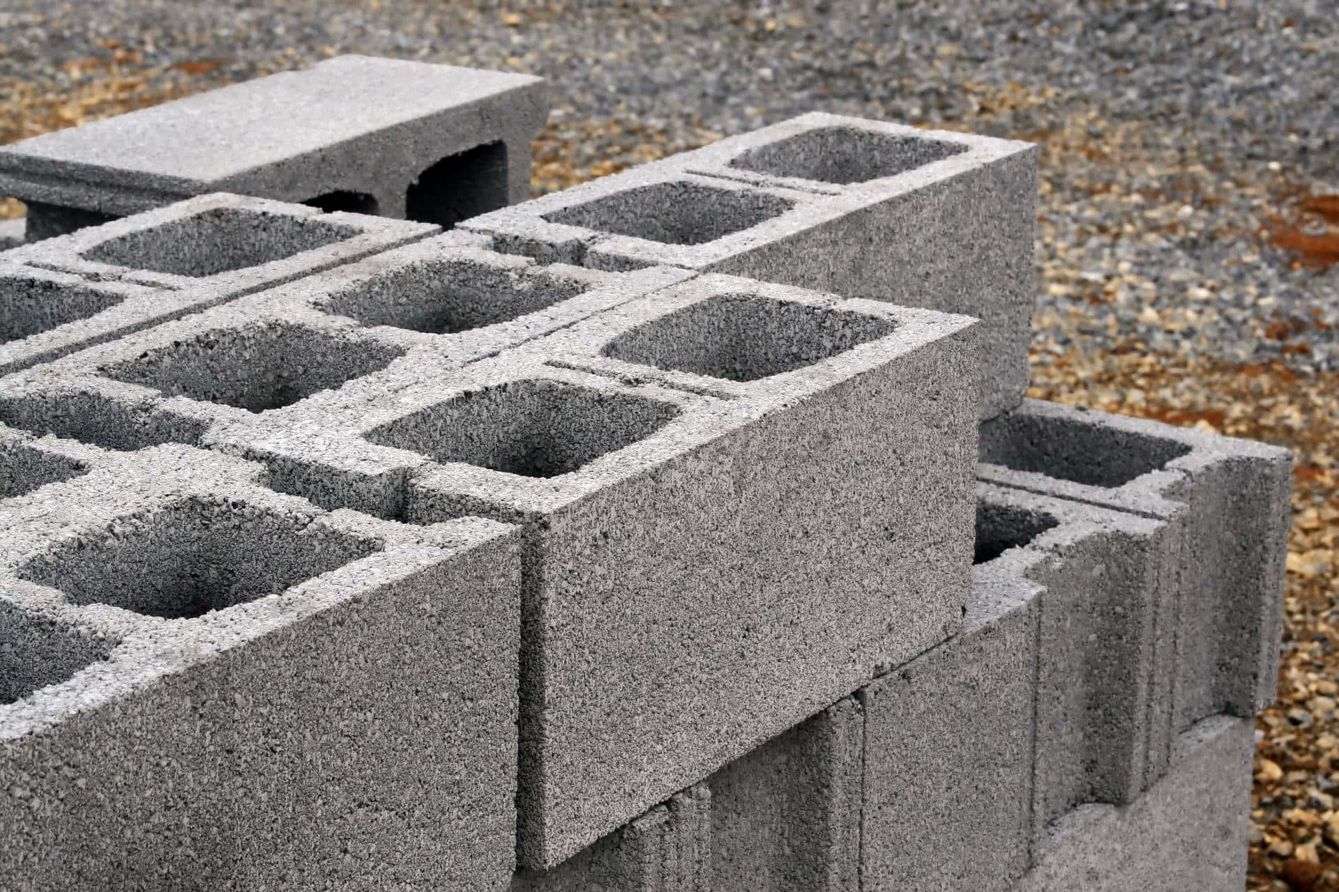 建築 桌布 壁紙 — 堆疊的灰色混凝土空心磚塊，空心核心，清晰地放置在礫石表面上。