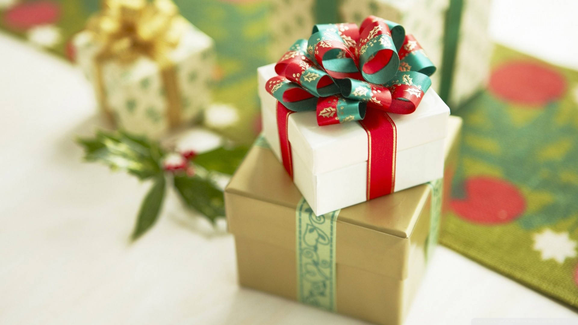 Presents 桌布 壁紙 — 堆疊的節日禮物，用喜慶的紅色、綠色和金色絲帶包裹，附近有冬青葉。