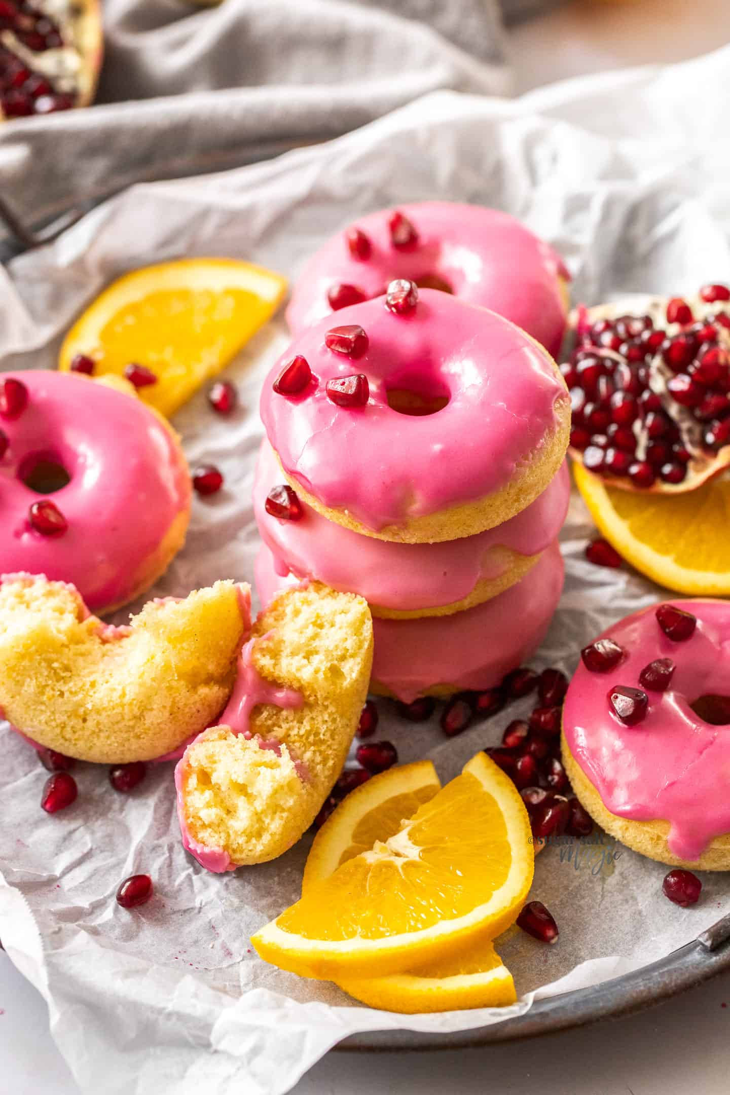 Donut 桌布 壁紙 — 堆疊的粉紅色糖霜甜甜圈，上面放有石榴籽和柳橙片，放在烘焙紙上。