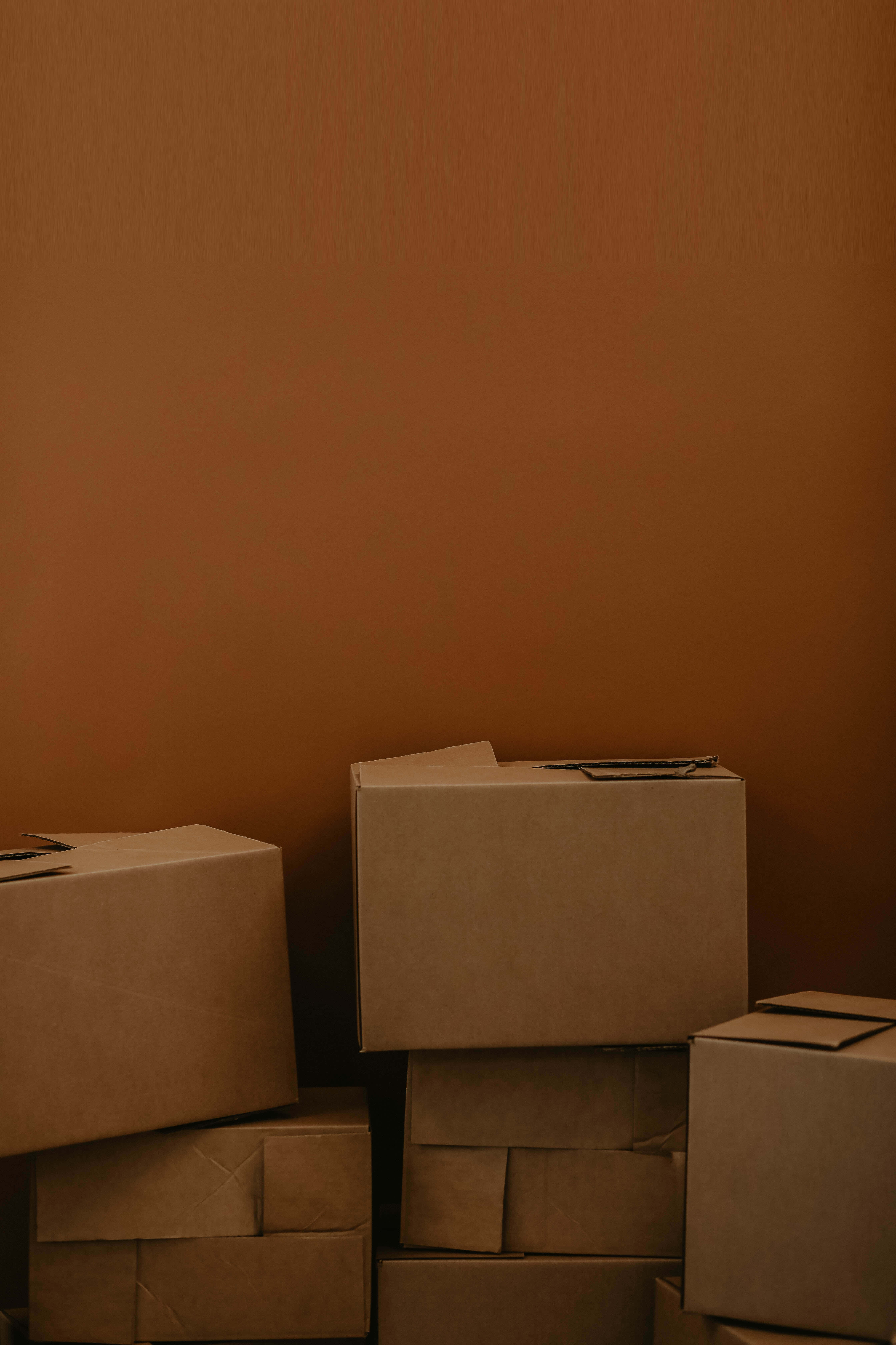 cardboard 桌布 壁紙 — 堆疊的紙箱靠著溫暖的赤陶牆，在一個簡約、光線昏暗的房間裡。