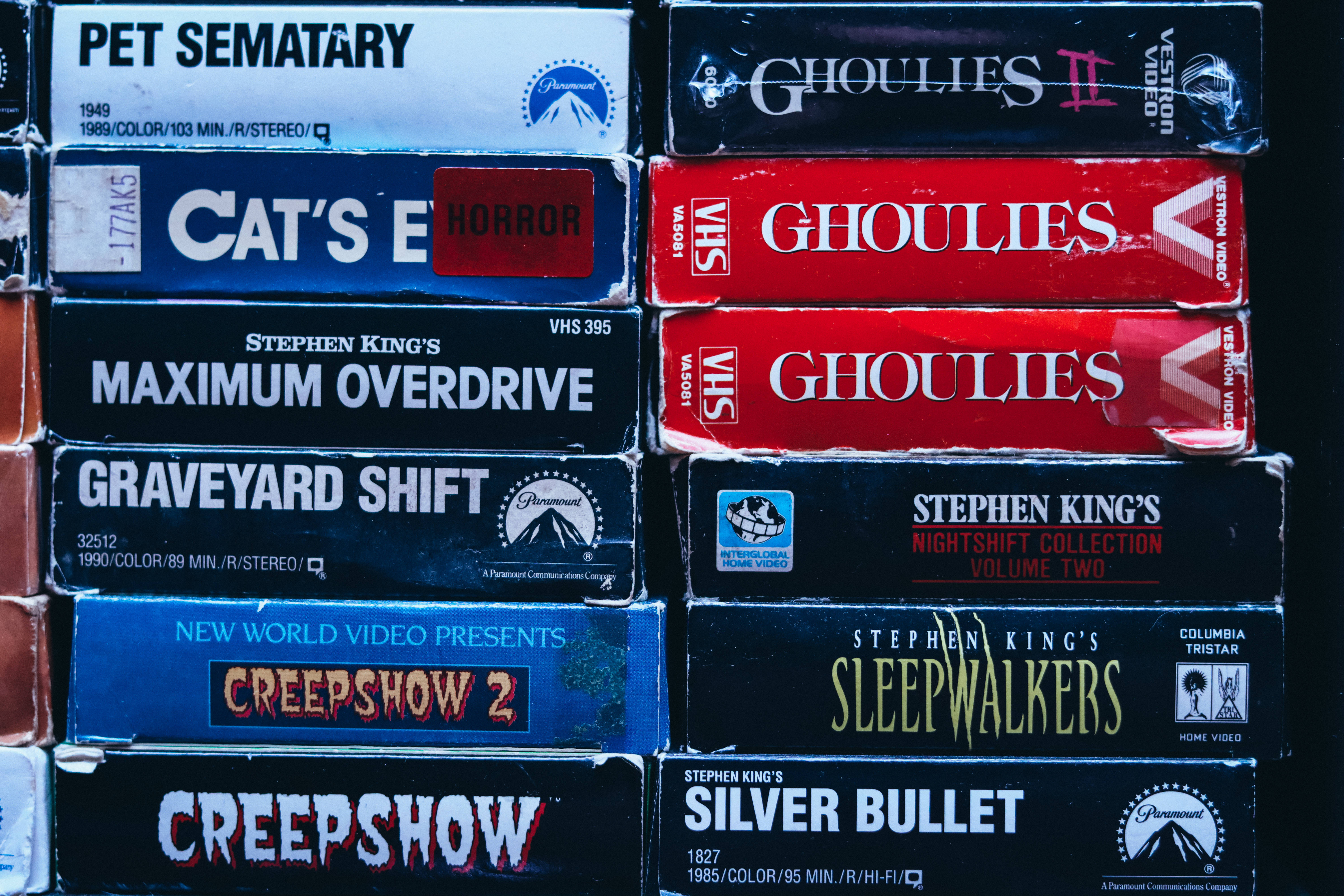Vintage Halloween 桌布 壁紙 — 堆疊的經典VHS錄影帶，如《寵物墳場》和《鬼娃》等史蒂芬·金恐怖電影，在戲劇性燈光下閃耀。
