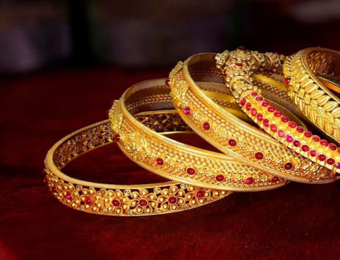 Bangles 桌布 壁紙 — 堆疊的華麗金手鐲，飾有紅色寶石，放置在深紅色天鵝絨表面上，光線柔和。