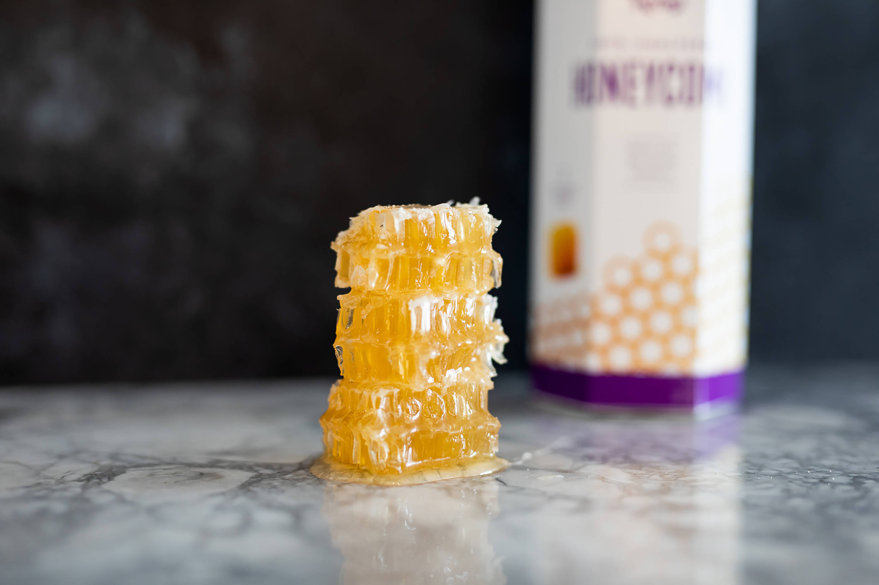 Honeycomb 桌布 壁紙 — 堆疊的金色蜂巢片在大理石表面上閃閃發光，旁邊放著一盒蜂蜜產品。