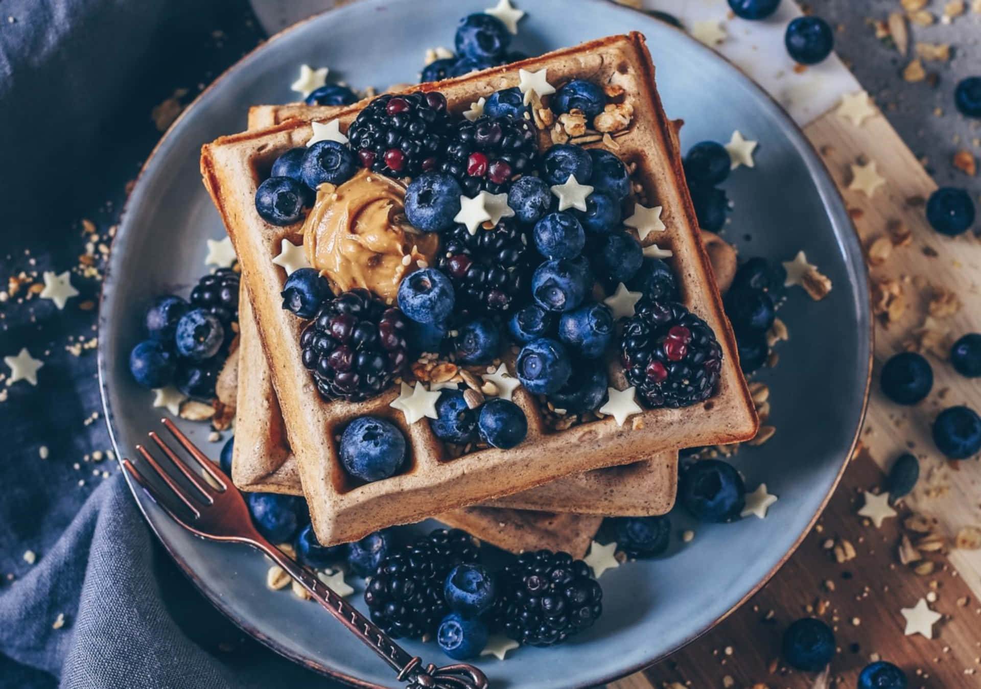 Waffle 桌布 壁紙 — 堆疊的金黃色鬆餅，上面放有藍莓、黑莓、花生醬和星形糖粒，放在藍色盤子上。