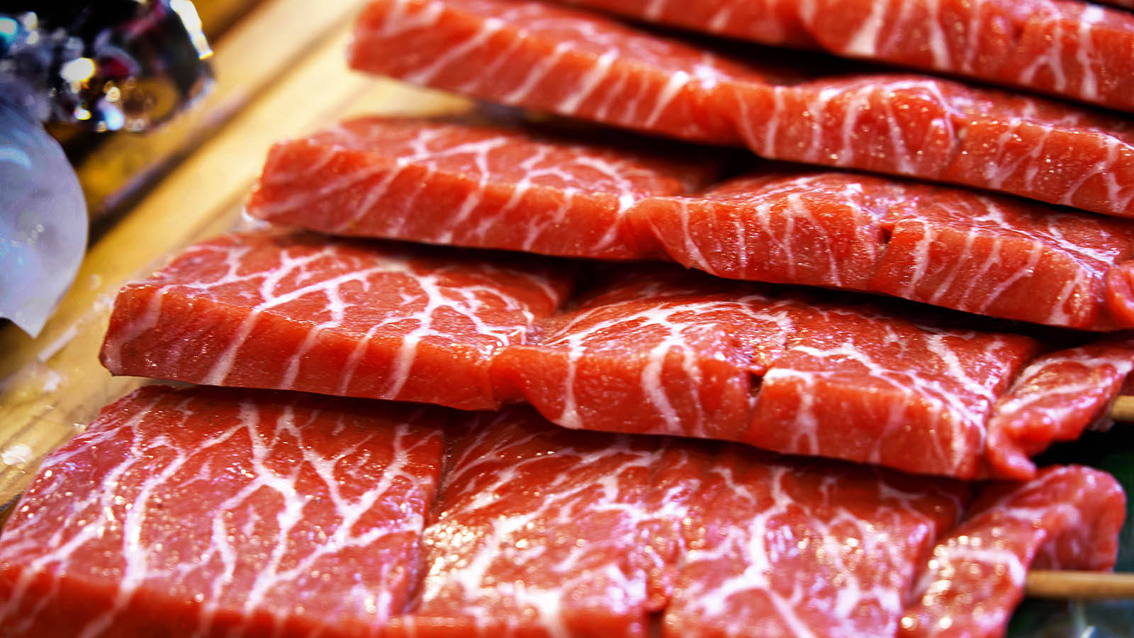 meat 桌布 壁紙 — 堆疊的雪花牛肉片，帶有白色脂肪紋理，在木質表面上於明亮光線下閃閃發光。
