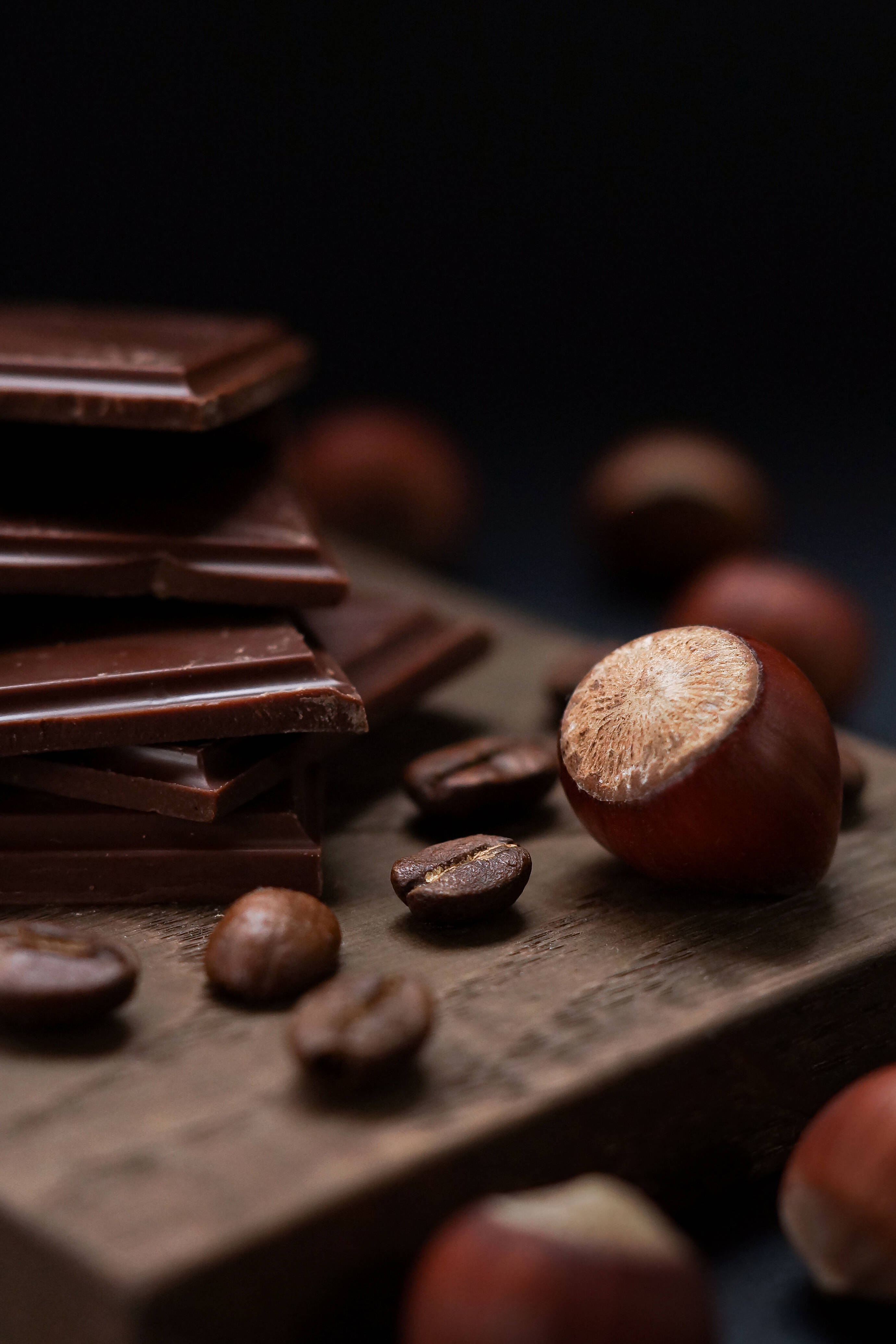 Chocolate 桌布 壁紙 — 堆疊的黑巧克力條和散落的咖啡豆與榛子放在深色背景的鄉村木板上。