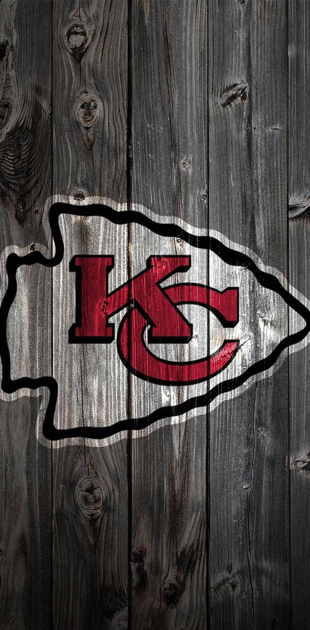 Kansas City Chiefs Logo 桌布 壁紙 — 堪薩斯城酋長隊標誌，紅白配色，位於風化灰色木板上，紋理和節疤清晰可見。