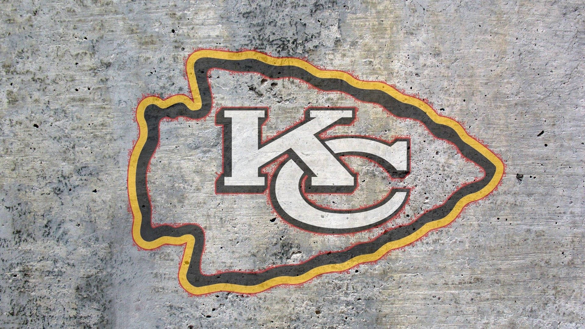 Kc Chiefs 桌布 壁紙 — 堪薩斯城酋長隊標誌以鮮明的黃色、黑色和白色繪製在風化的灰色混凝土牆上。